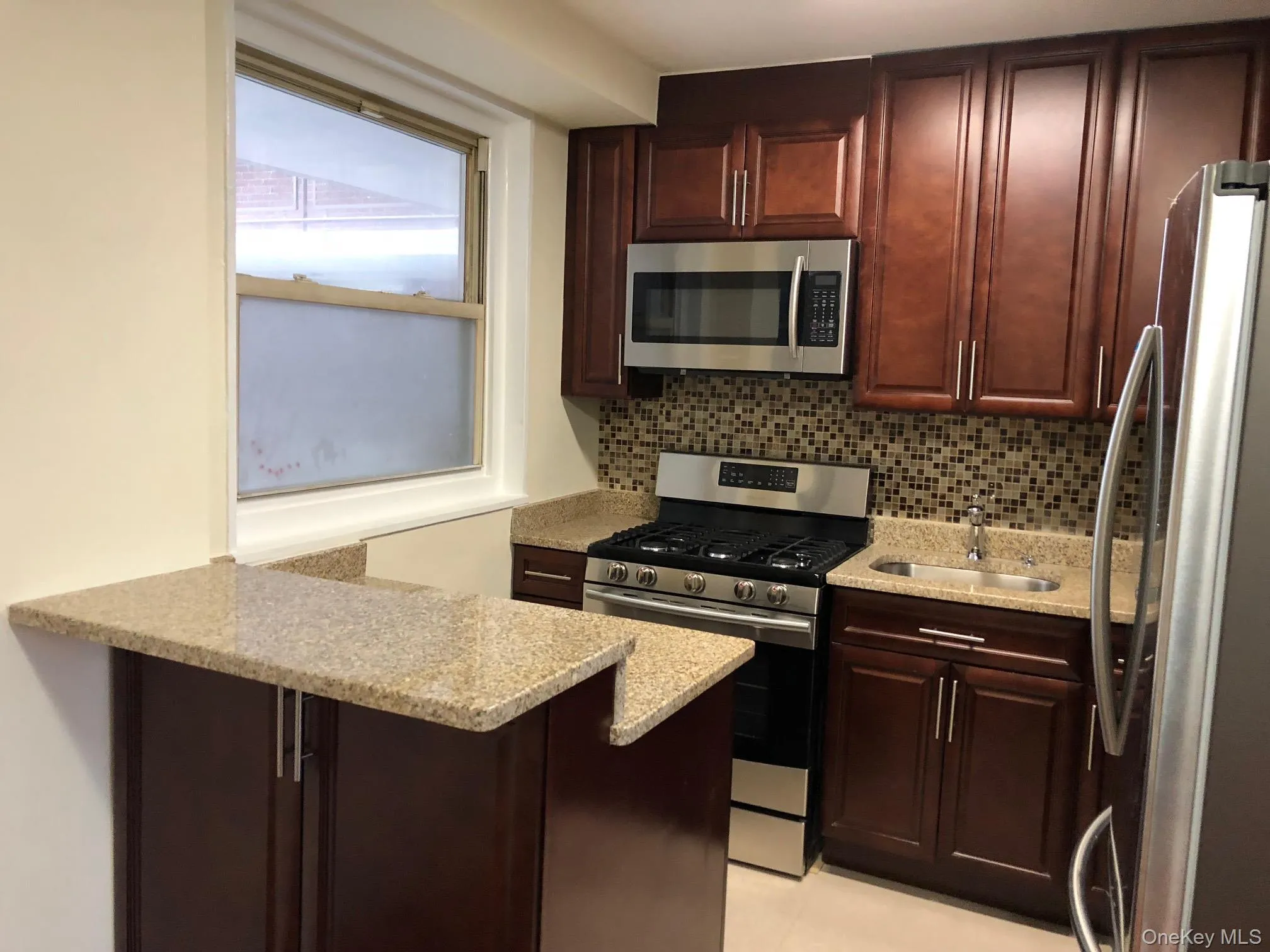 Kitchen with stainless steel appliances, tasteful backsplash, light stone counters, and a peninsula Kitchen with stainless steel appliances, tasteful backsplash, light stone counters, and a peninsula