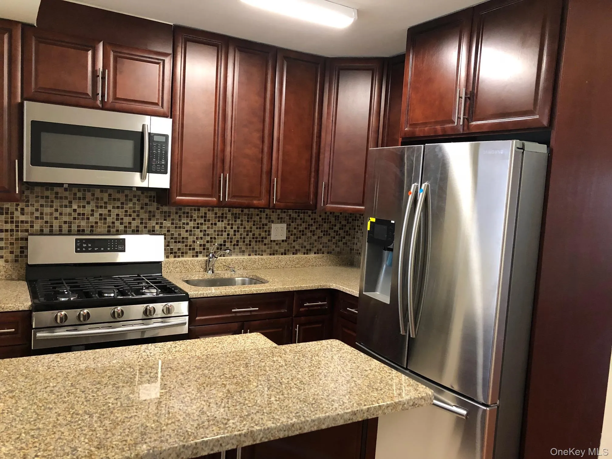 Kitchen with appliances with stainless steel finishes, light stone counters, tasteful backsplash, and dark brown cabinetry Kitchen with appliances with stainless steel finishes, light stone counters, tasteful backsplash, and dark brown cabinetry