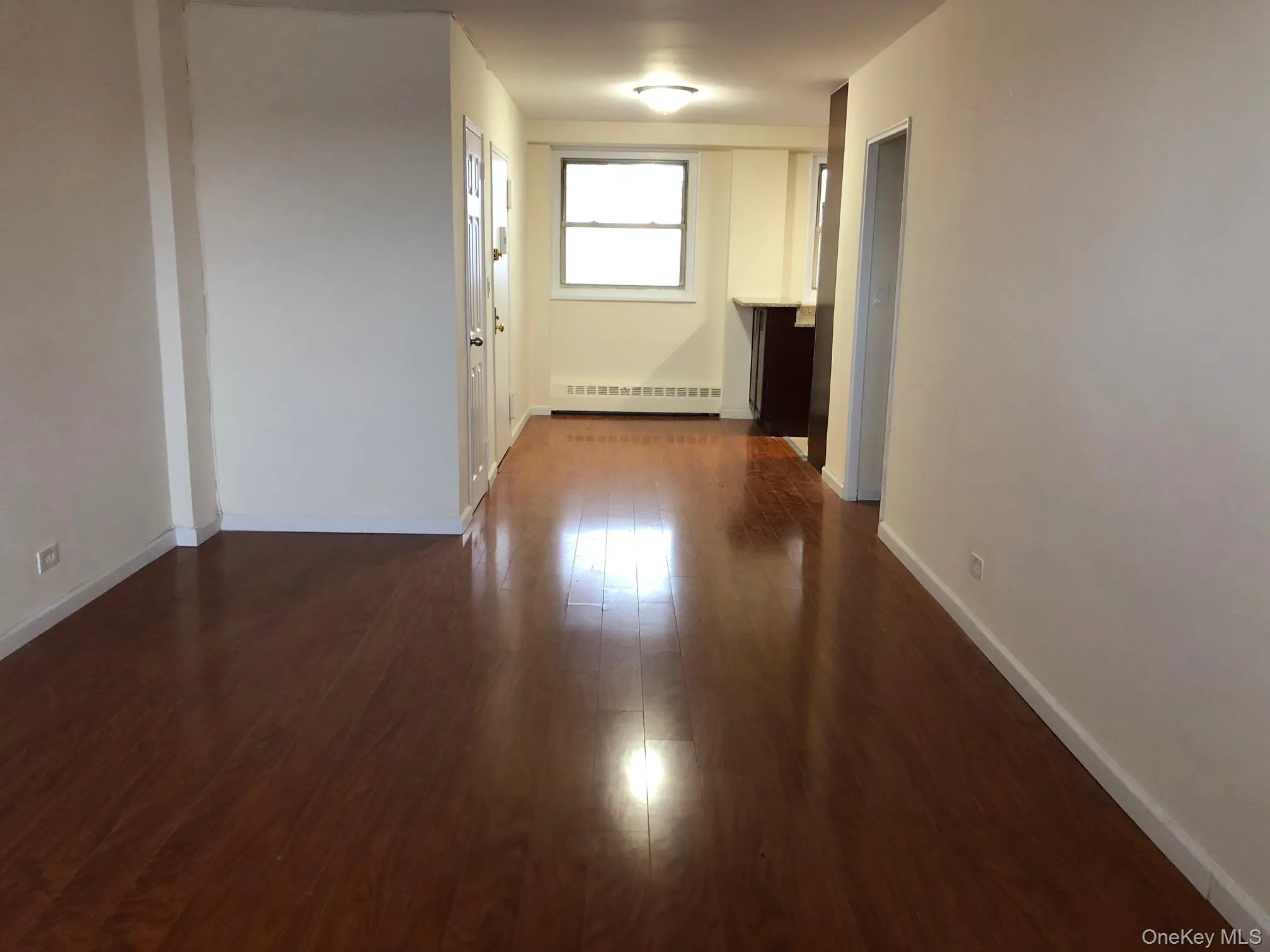 Hallway with dark wood-style flooring and a baseboard radiator Hallway with dark wood-style flooring and a baseboard radiator