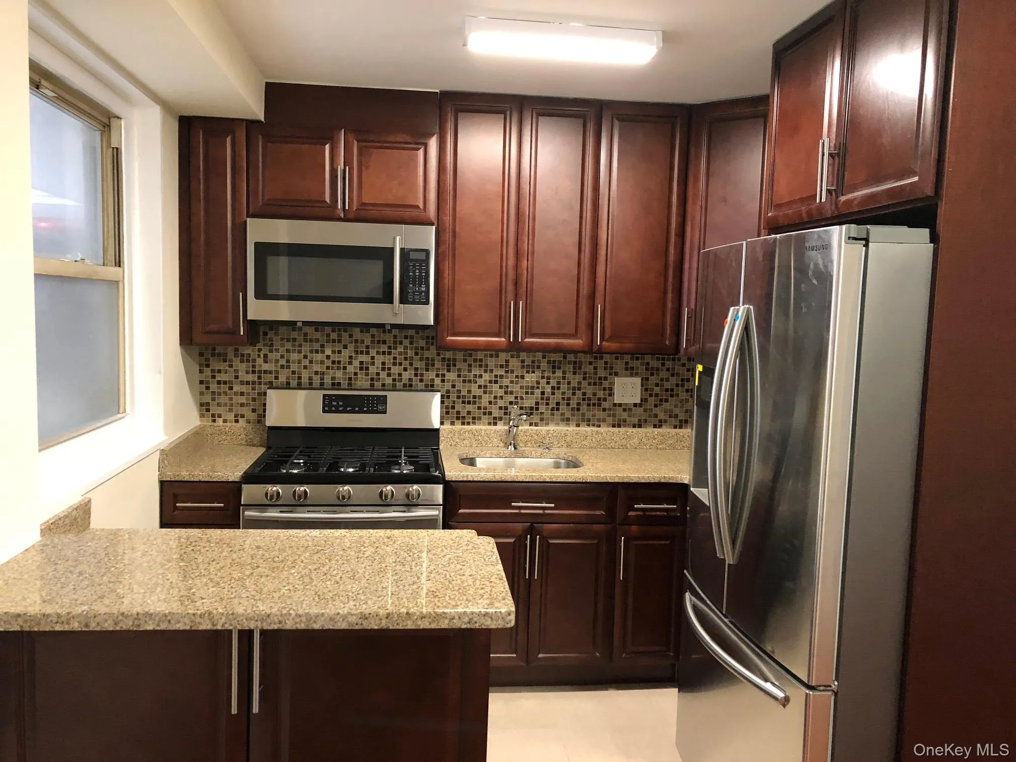 Kitchen featuring appliances with stainless steel finishes, light stone counters, a peninsula, backsplash, and dark brown cabinetry Kitchen featuring appliances with stainless steel finishes, light stone counters, a peninsula, backsplash, and dark brown cabinetry