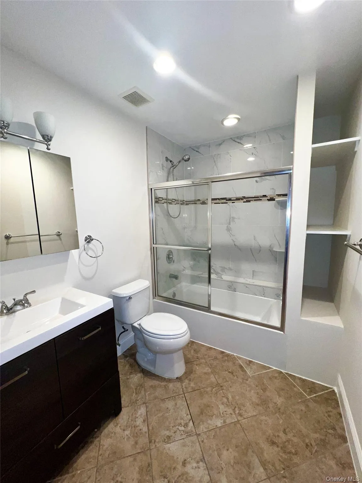 Full bathroom featuring bath / shower combo with glass door, vanity, and light tile patterned floors Full bathroom featuring bath / shower combo with glass door, vanity, and light tile patterned floors