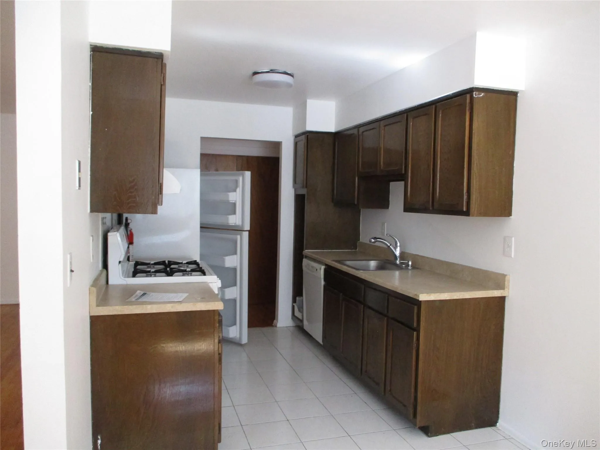 Kitchen featuring light countertops, white appliances, dark brown cabinets, and light tile patterned floors Kitchen featuring light countertops, white appliances, dark brown cabinets, and light tile patterned floors
