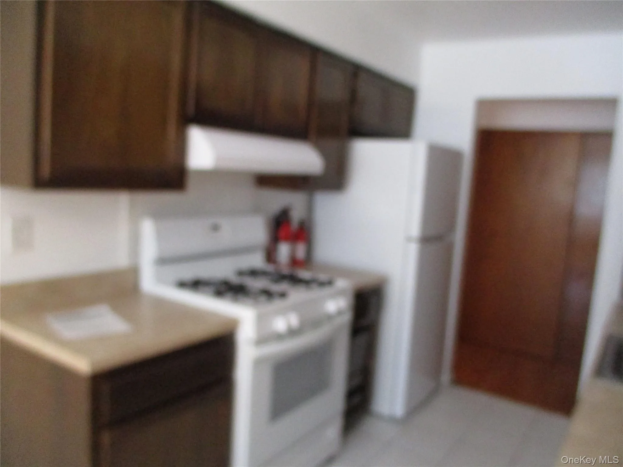 Kitchen with white appliances, extractor fan, dark brown cabinetry, light countertops, and light tile patterned floors Kitchen with white appliances, extractor fan, dark brown cabinetry, light countertops, and light tile patterned floors