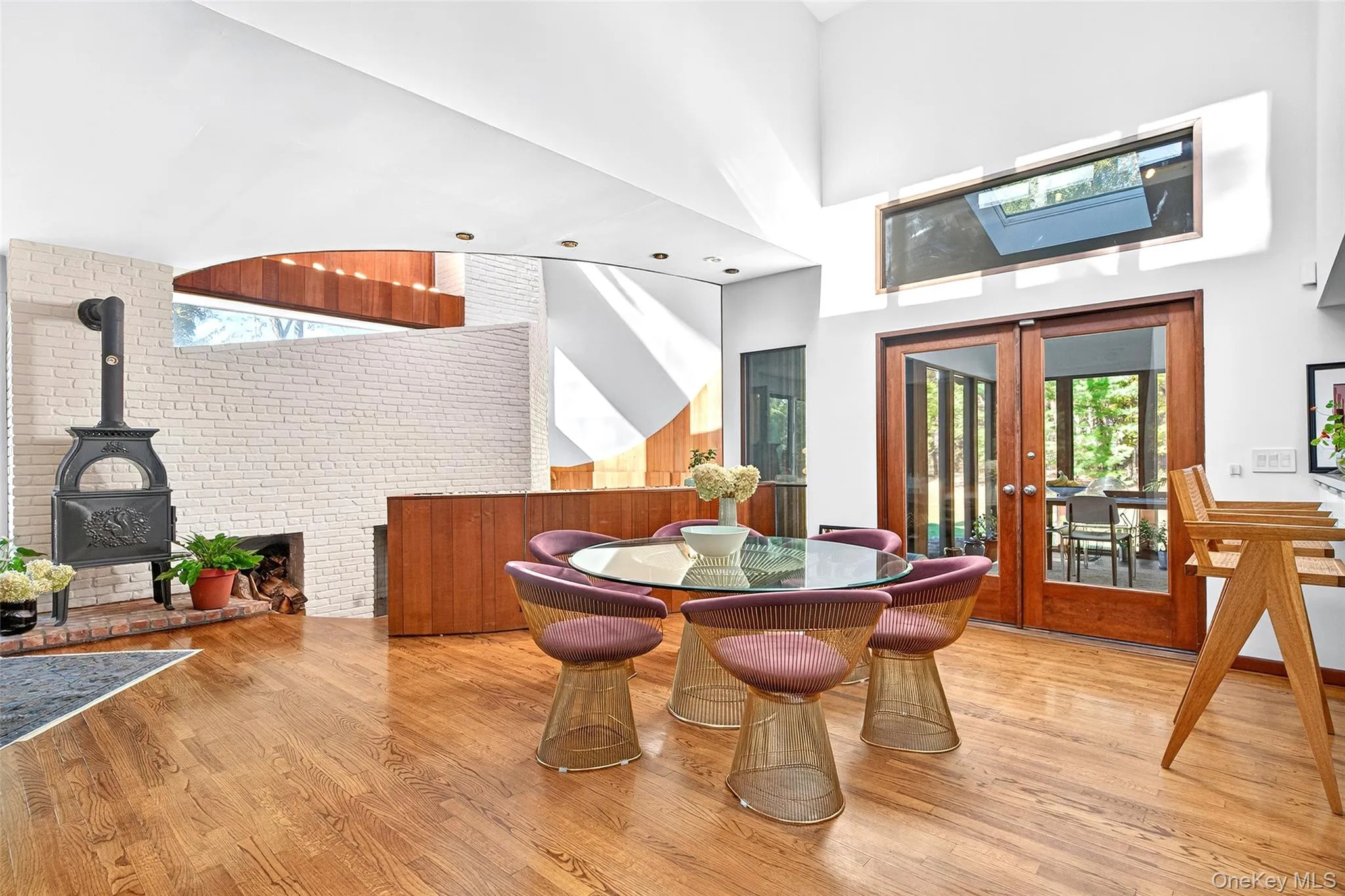 Great Room featuring wood finished floors, a towering ceiling, french doors, a wood stove, and brick wall with fireplace. Great Room featuring wood finished floors, a towering ceiling, french doors, a wood stove, and brick wall with fireplace.