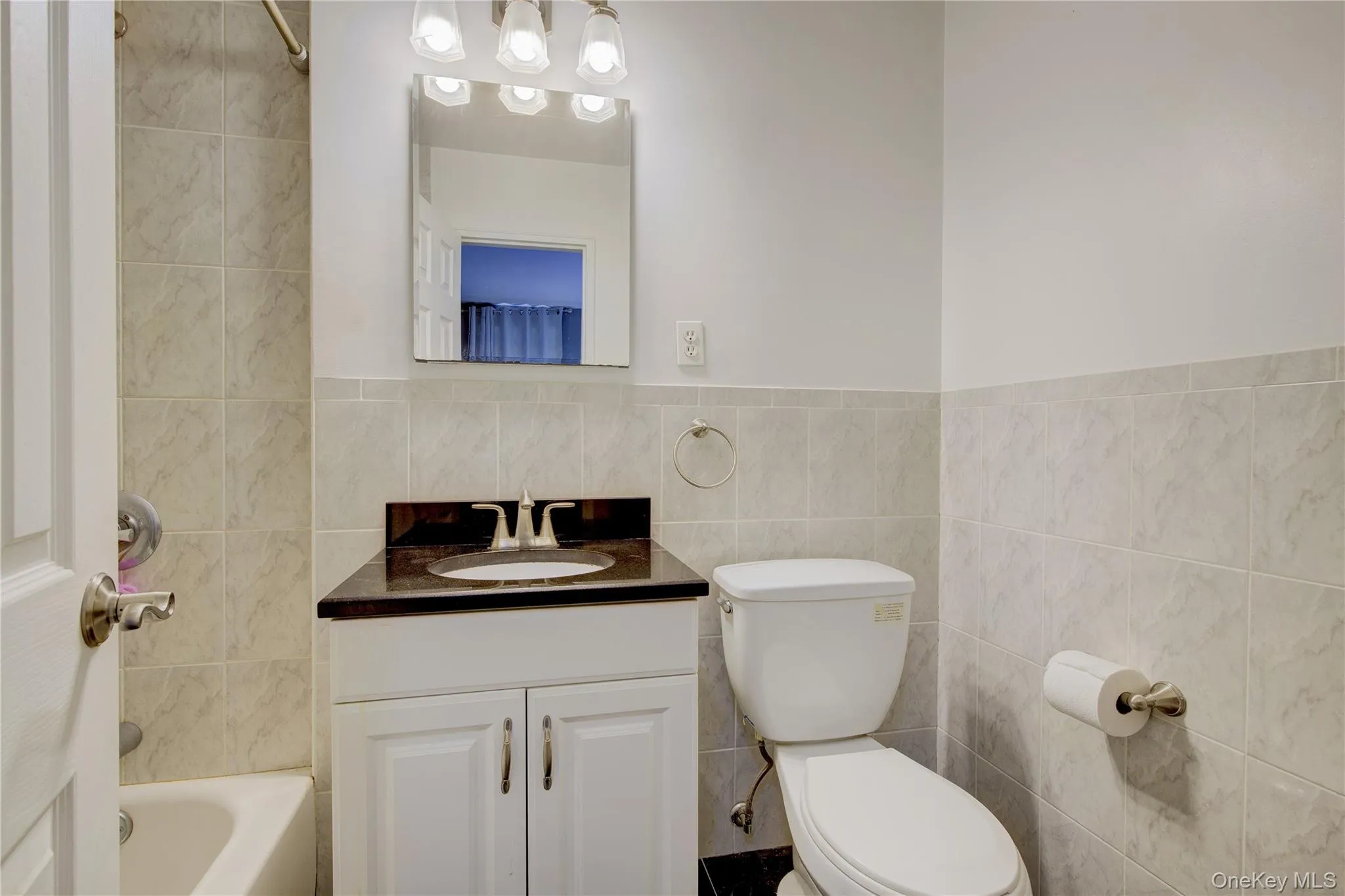 Full bath with vanity, shower / bath combo, tile walls, and a wainscoted wall Full bath with vanity, shower / bath combo, tile walls, and a wainscoted wall