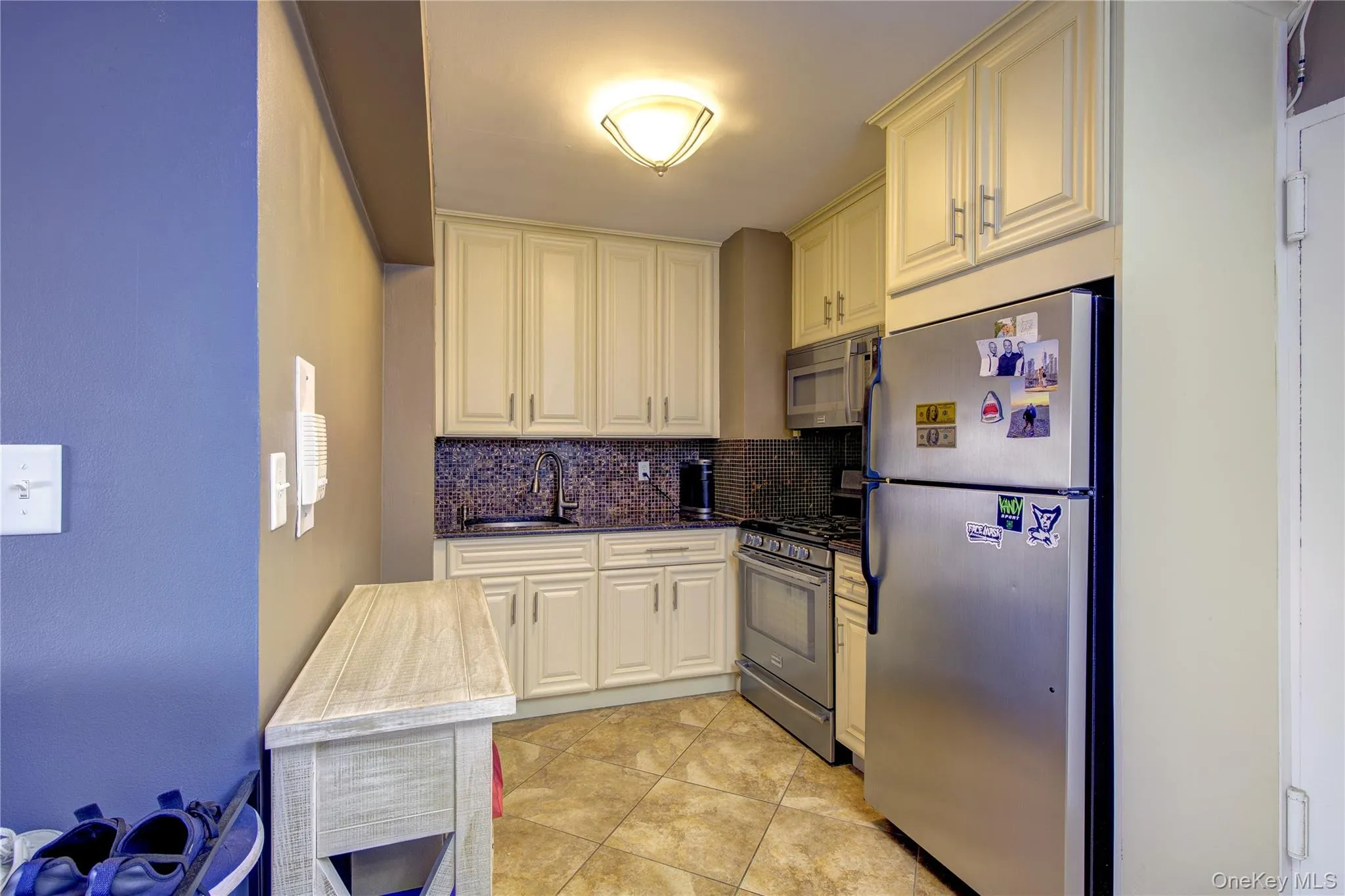 Kitchen featuring stainless steel appliances, tasteful backsplash, cream cabinetry, light tile patterned flooring, and dark stone counters Kitchen featuring stainless steel appliances, tasteful backsplash, cream cabinetry, light tile patterned flooring, and dark stone counters