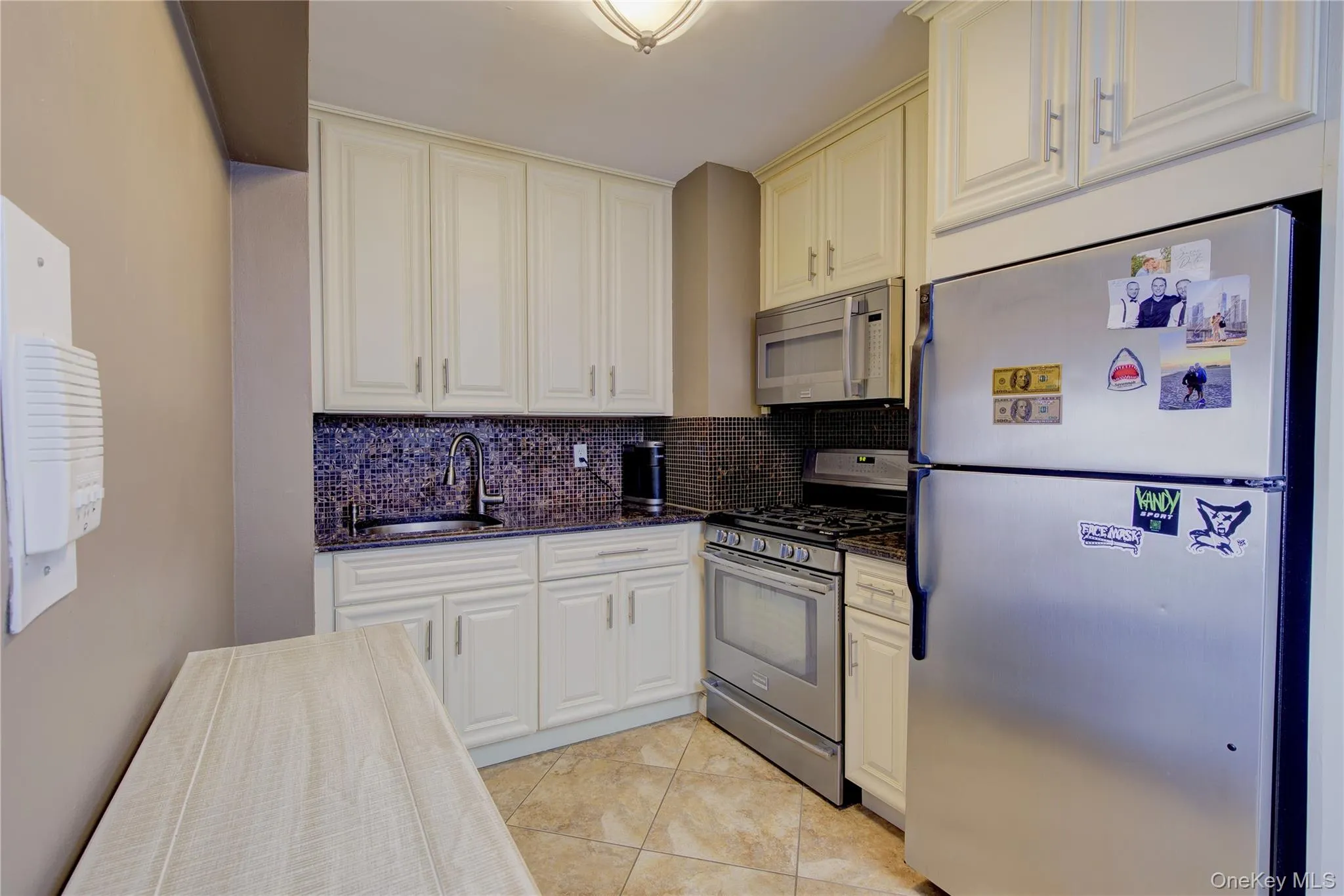 Kitchen with stainless steel appliances, decorative backsplash, dark stone counters, and light tile patterned flooring Kitchen with stainless steel appliances, decorative backsplash, dark stone counters, and light tile patterned flooring