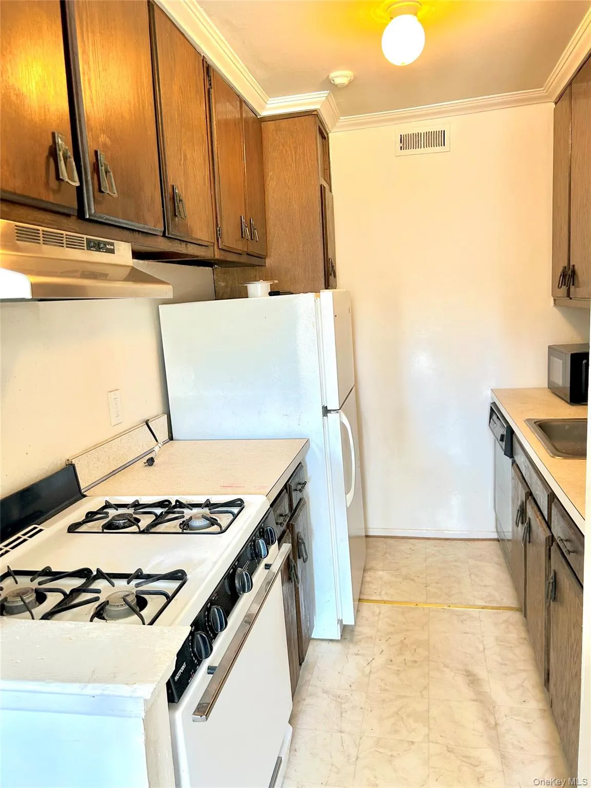 Kitchen featuring light countertops, white appliances, crown molding, under cabinet range hood, and brown cabinetry Kitchen featuring light countertops, white appliances, crown molding, under cabinet range hood, and brown cabinetry