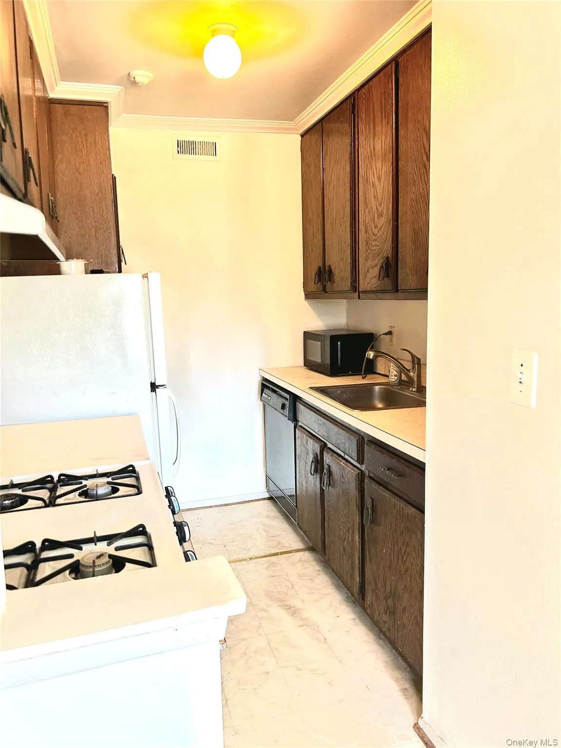Kitchen with light countertops, dark brown cabinets, white appliances, ornamental molding, and under cabinet range hood Kitchen with light countertops, dark brown cabinets, white appliances, ornamental molding, and under cabinet range hood