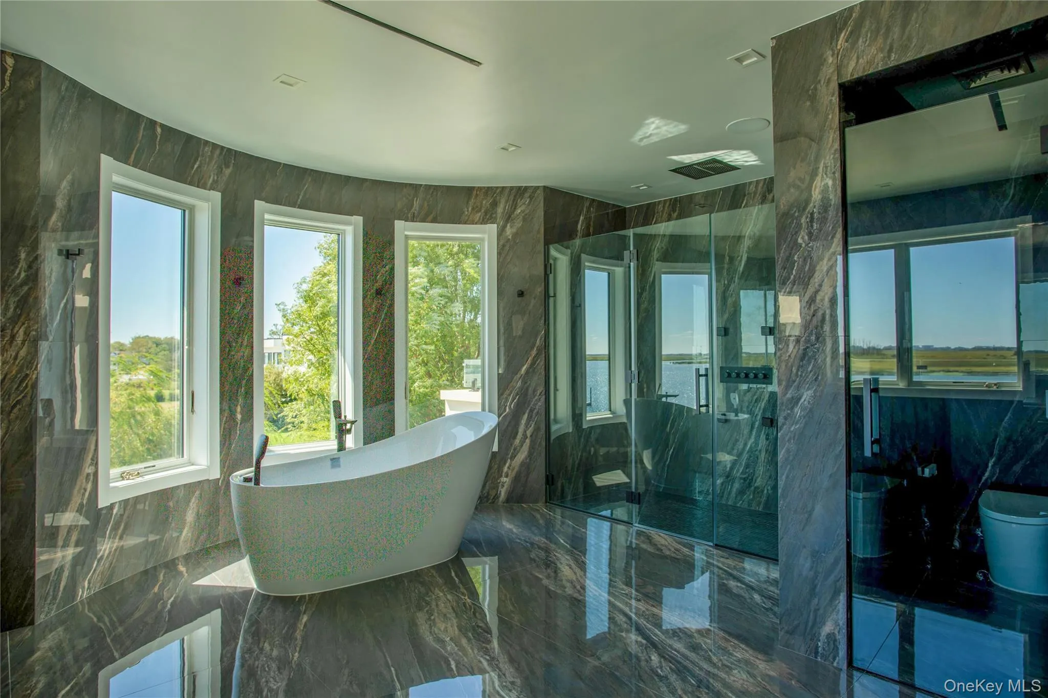 Full bath with dark marble finish flooring, a freestanding bath, a marble finish shower, and tile walls Full bath with dark marble finish flooring, a freestanding bath, a marble finish shower, and tile walls