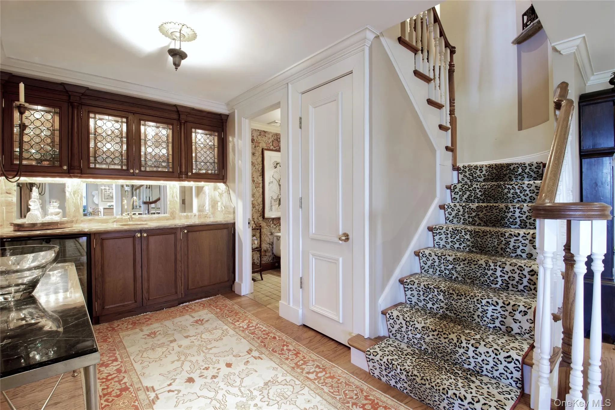 Bar area with stairway, glass insert cabinets, ornamental molding, dark brown cabinetry, and light stone counters Bar area with stairway, glass insert cabinets, ornamental molding, dark brown cabinetry, and light stone counters