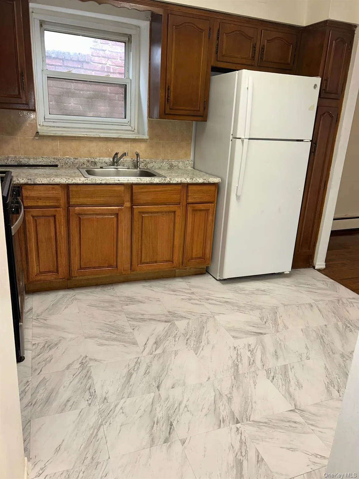 Kitchen with freestanding refrigerator, light countertops, black range oven, and brown cabinets Kitchen with freestanding refrigerator, light countertops, black range oven, and brown cabinets