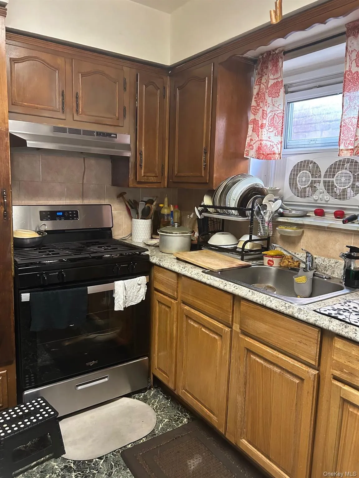 Kitchen featuring stainless steel gas stove, under cabinet range hood, brown cabinetry, and backsplash Kitchen featuring stainless steel gas stove, under cabinet range hood, brown cabinetry, and backsplash