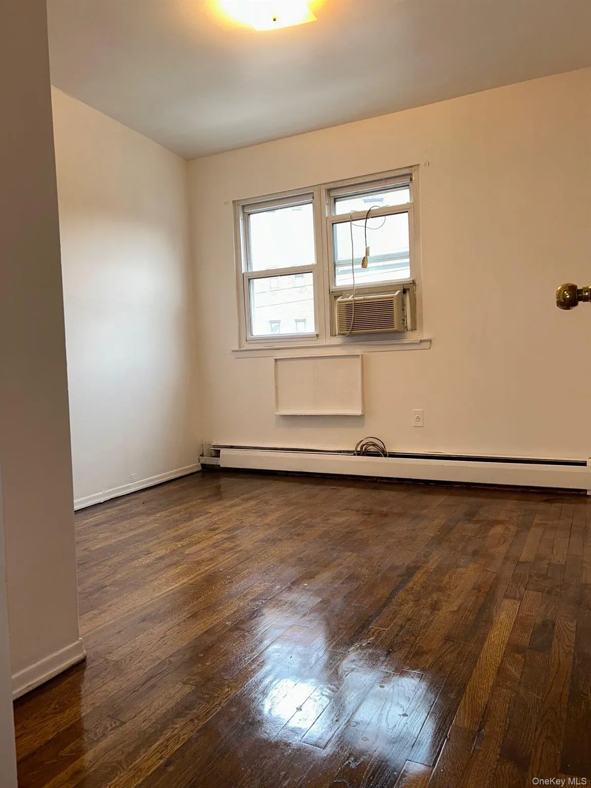 Empty room featuring baseboard heating, dark wood-style flooring, and cooling unit Empty room featuring baseboard heating, dark wood-style flooring, and cooling unit