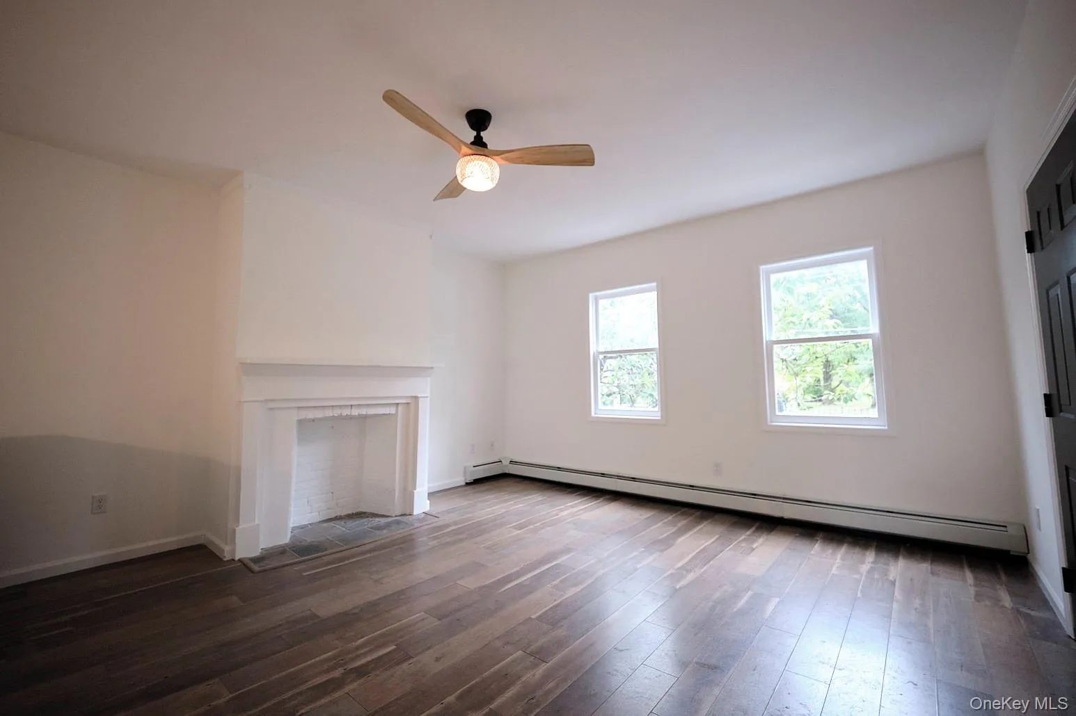 Unfurnished living room featuring dark wood finished floors, a baseboard heating unit, a ceiling fan, and a fireplace with flush hearth Unfurnished living room featuring dark wood finished floors, a baseboard heating unit, a ceiling fan, and a fireplace with flush hearth