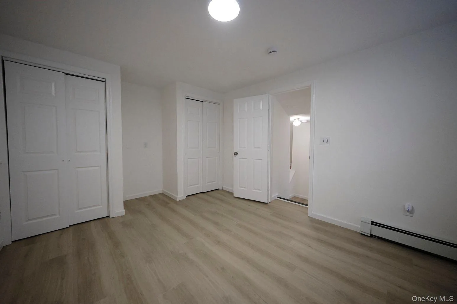 Unfurnished bedroom featuring multiple closets, light wood-type flooring, and baseboard heating Unfurnished bedroom featuring multiple closets, light wood-type flooring, and baseboard heating