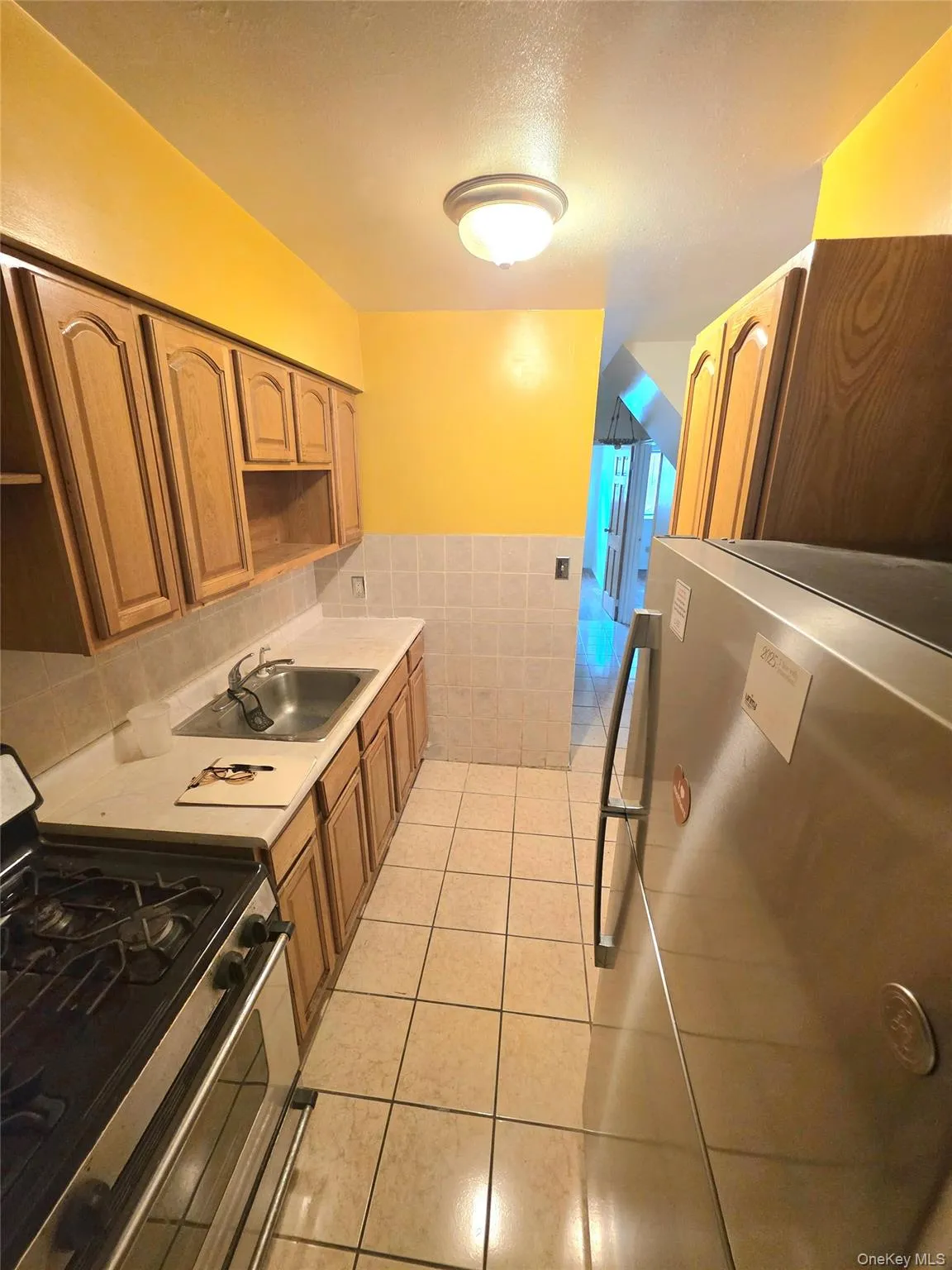 Kitchen with stainless steel appliances, light countertops, light tile patterned flooring, brown cabinetry, and tile walls Kitchen with stainless steel appliances, light countertops, light tile patterned flooring, brown cabinetry, and tile walls