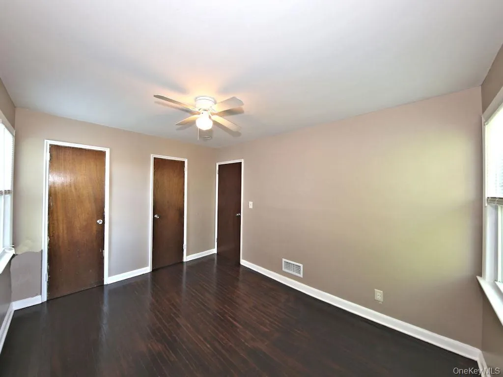 Unfurnished bedroom featuring multiple windows, dark wood-type flooring, two closets, and ceiling fan Unfurnished bedroom featuring multiple windows, dark wood-type flooring, two closets, and ceiling fan