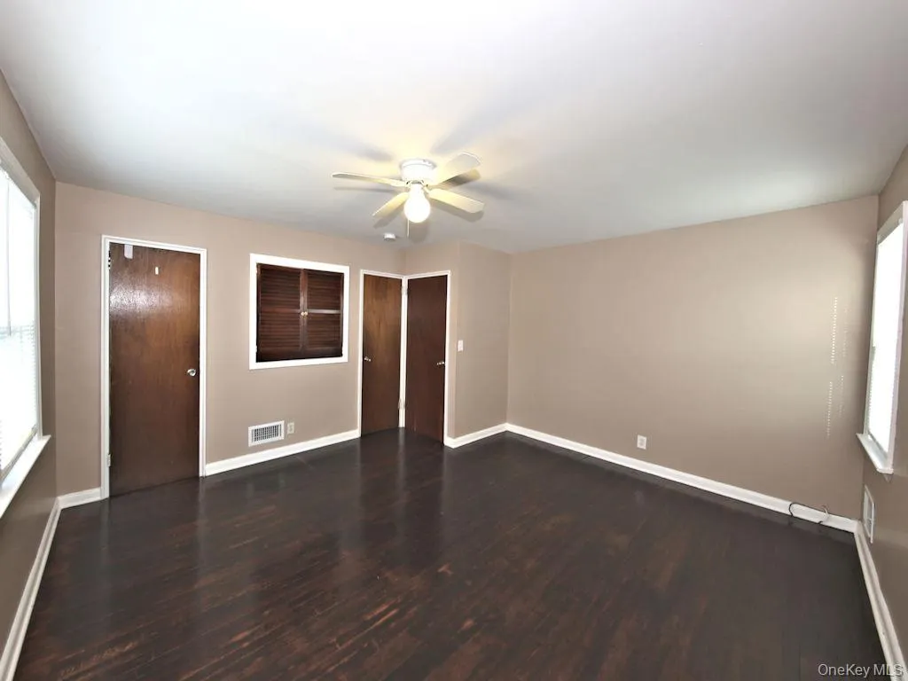 Spare room featuring plenty of natural light, dark wood-style flooring, and ceiling fan Spare room featuring plenty of natural light, dark wood-style flooring, and ceiling fan