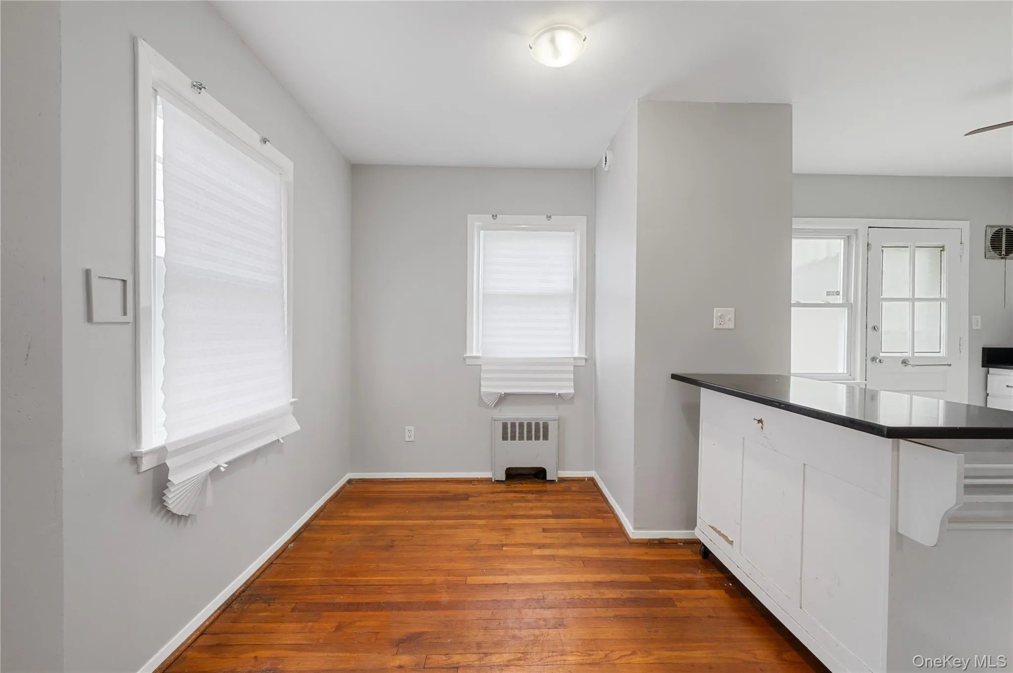 Kitchen with dark countertops, white cabinets, dark wood-style floors, and radiator Kitchen with dark countertops, white cabinets, dark wood-style floors, and radiator
