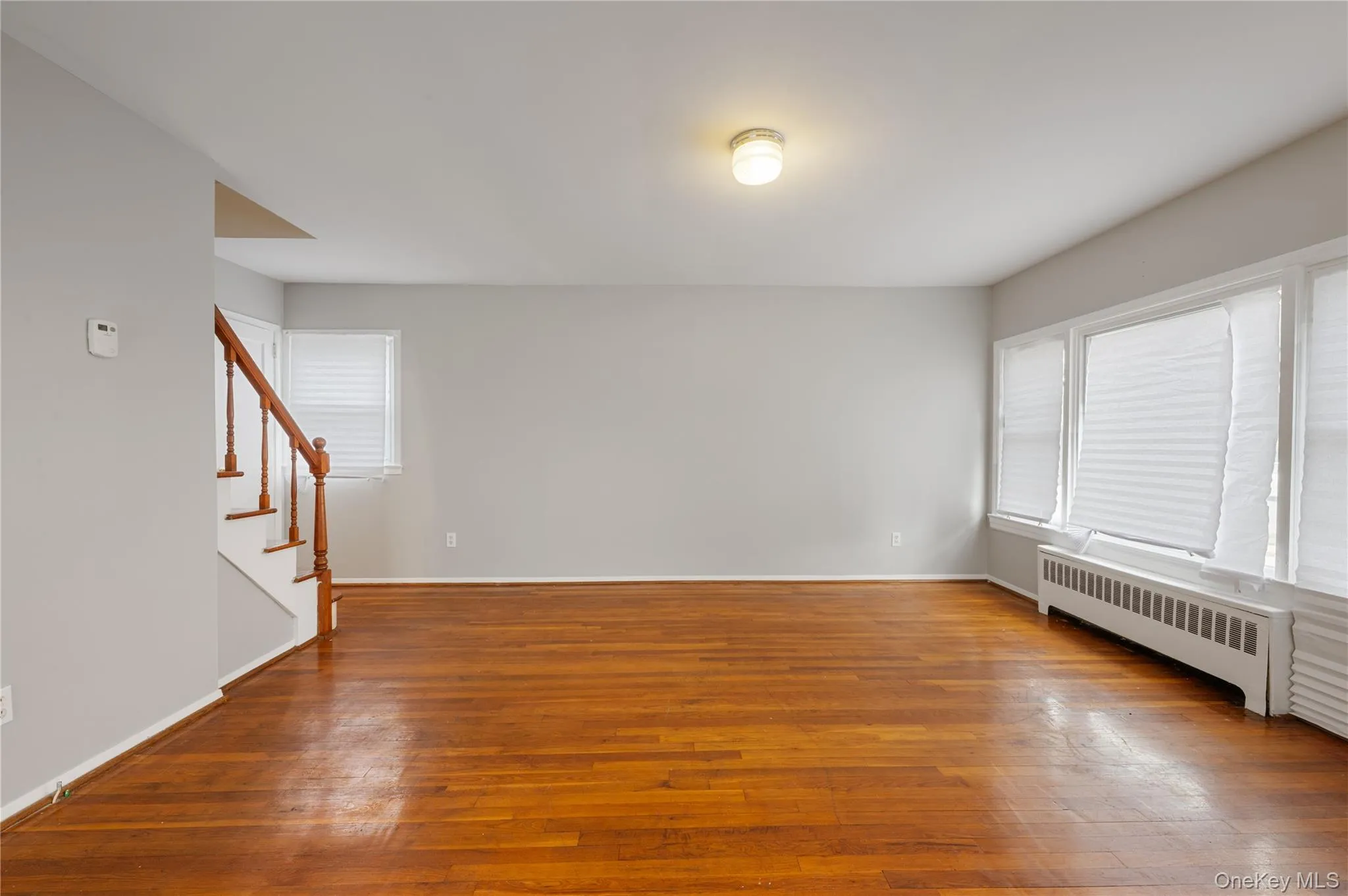 Unfurnished room featuring radiator heating unit, light wood-type flooring, and stairway Unfurnished room featuring radiator heating unit, light wood-type flooring, and stairway