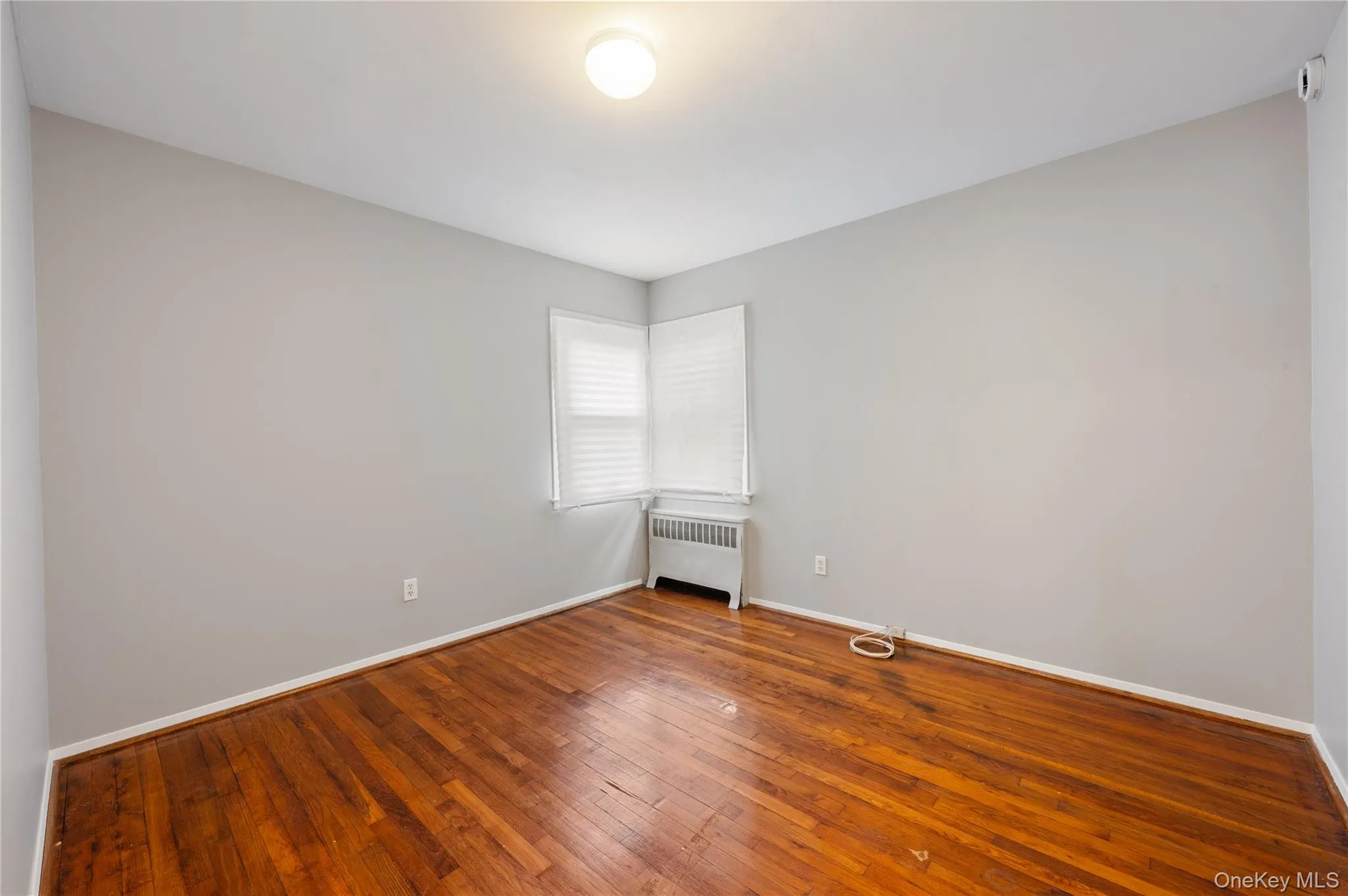Unfurnished room with hardwood / wood-style floors and radiator heating unit Unfurnished room with hardwood / wood-style floors and radiator heating unit