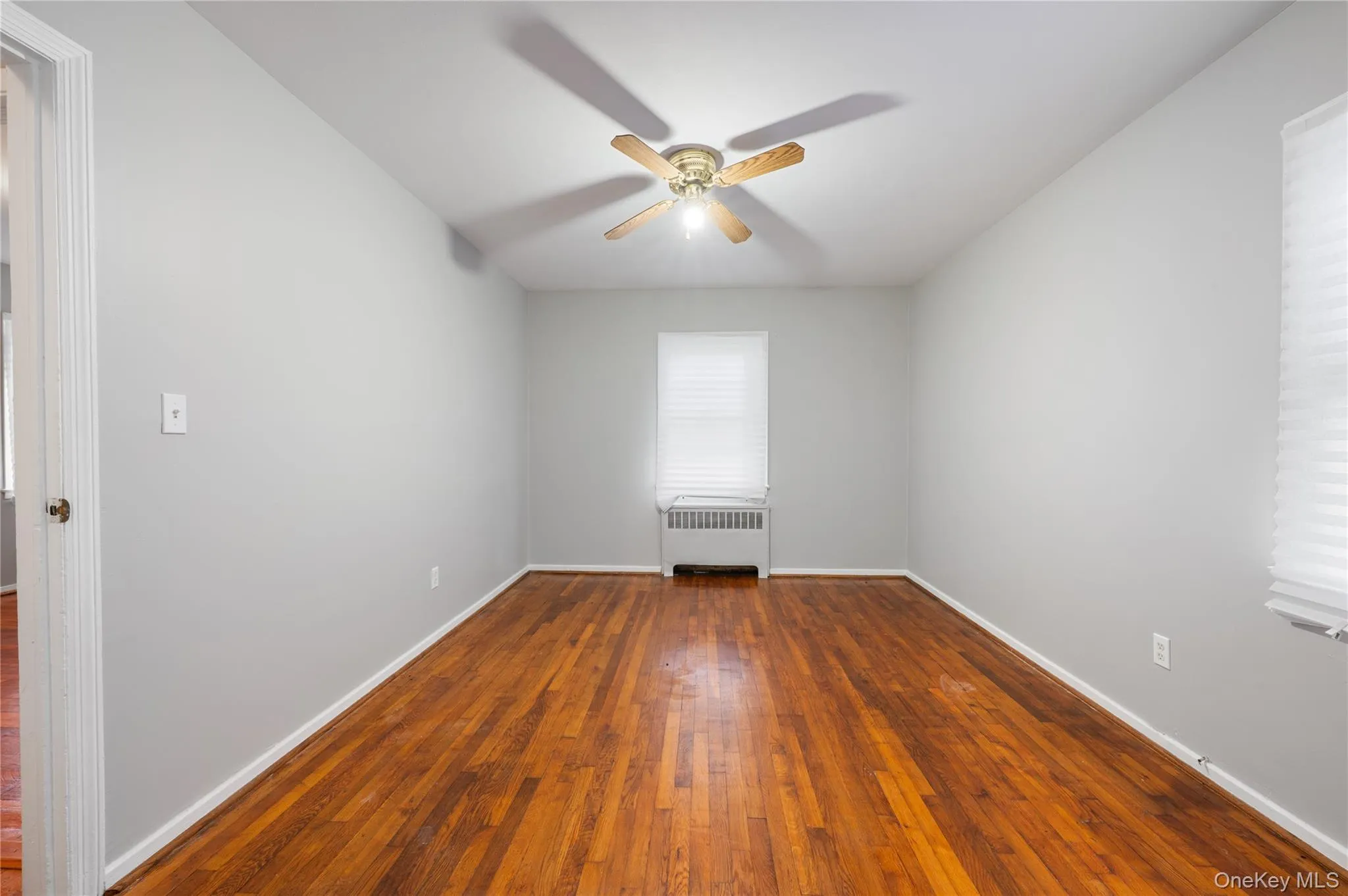 Unfurnished room featuring dark wood-style floors, radiator, ceiling fan, and healthy amount of natural light Unfurnished room featuring dark wood-style floors, radiator, ceiling fan, and healthy amount of natural light