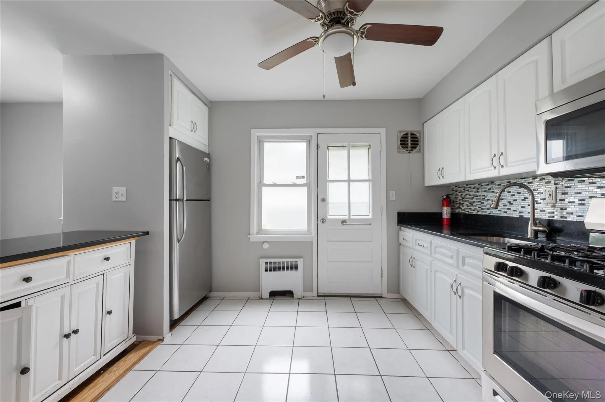 Kitchen with appliances with stainless steel finishes, radiator, tasteful backsplash, white cabinets, and dark stone counters Kitchen with appliances with stainless steel finishes, radiator, tasteful backsplash, white cabinets, and dark stone counters