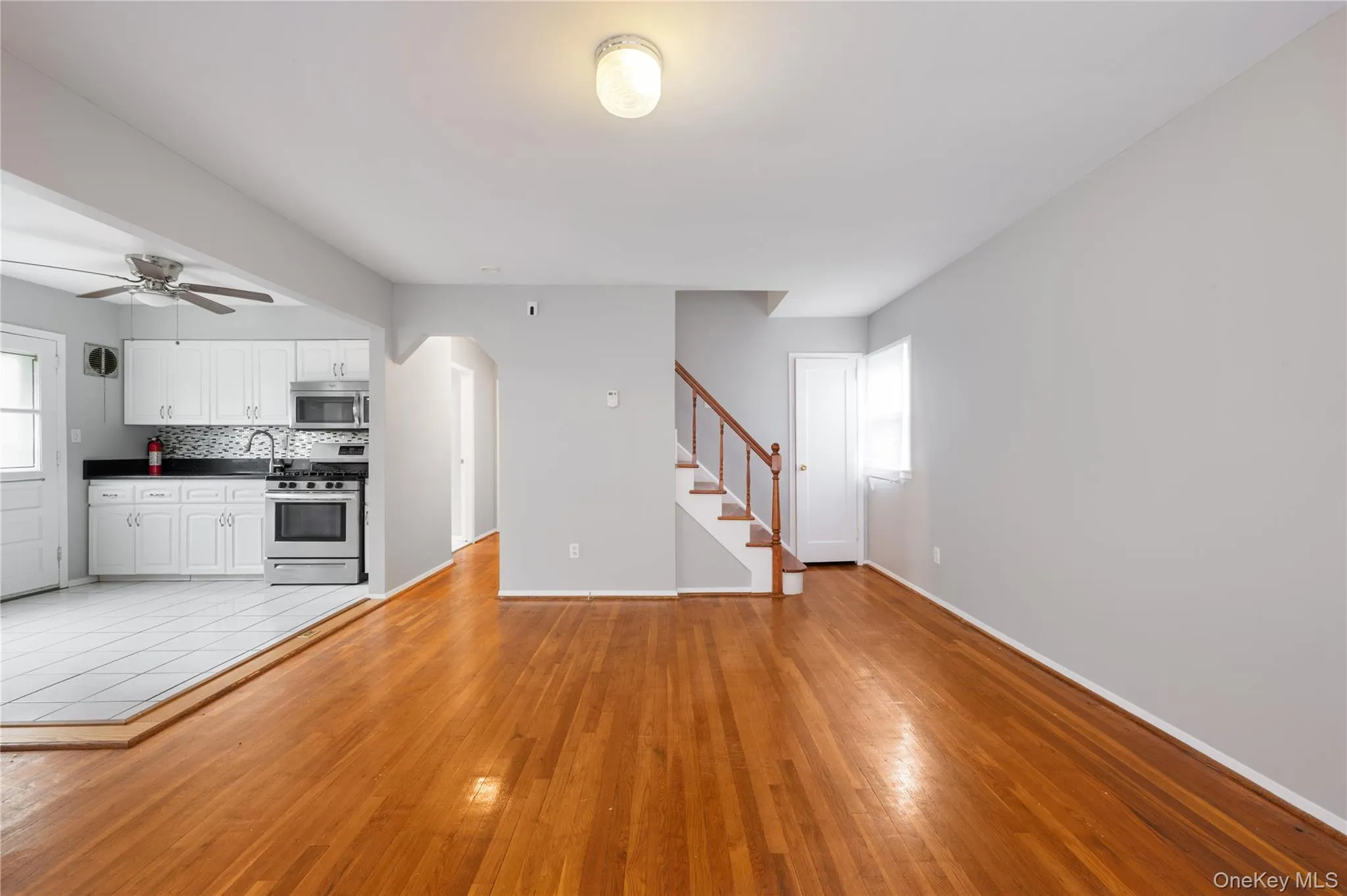 Unfurnished living room featuring arched walkways, light wood finished floors, stairs, and a ceiling fan Unfurnished living room featuring arched walkways, light wood finished floors, stairs, and a ceiling fan
