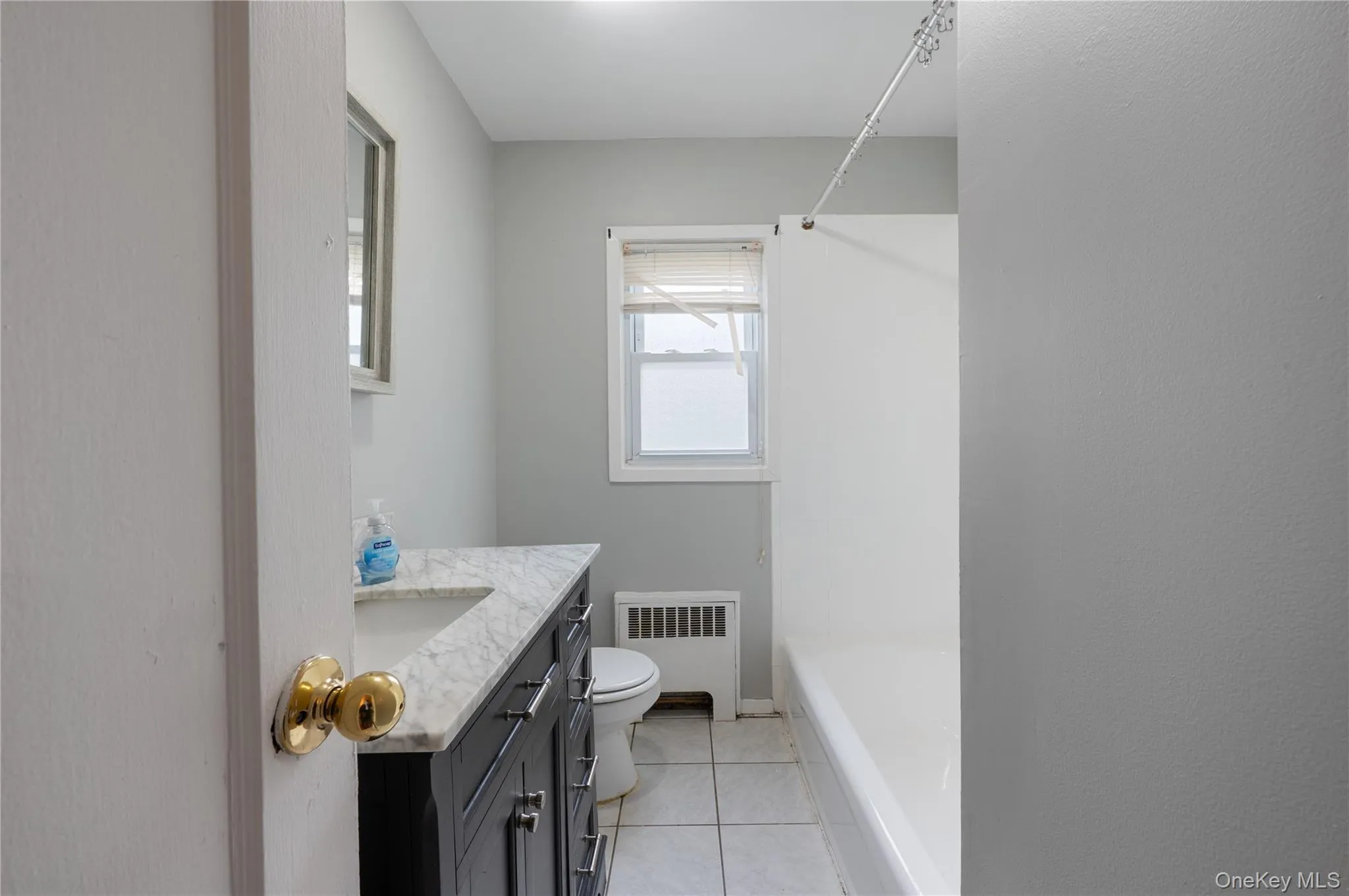 Bathroom featuring vanity, light tile patterned floors, radiator heating unit, and shower / bath combination Bathroom featuring vanity, light tile patterned floors, radiator heating unit, and shower / bath combination
