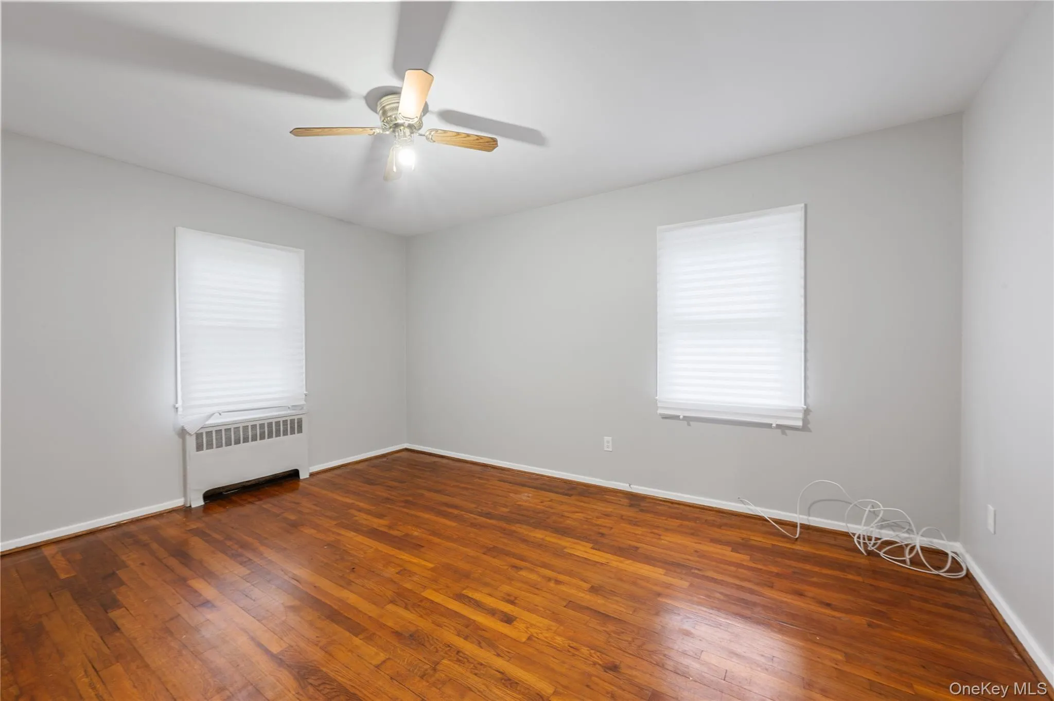 Spare room with radiator heating unit, dark wood-style flooring, and a ceiling fan Spare room with radiator heating unit, dark wood-style flooring, and a ceiling fan