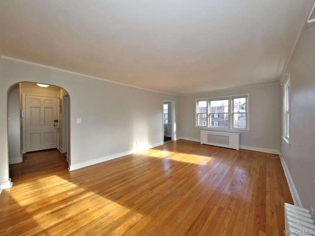 Unfurnished room featuring light wood-style flooring, radiator heating unit, arched walkways, and crown molding Unfurnished room featuring light wood-style flooring, radiator heating unit, arched walkways, and crown molding