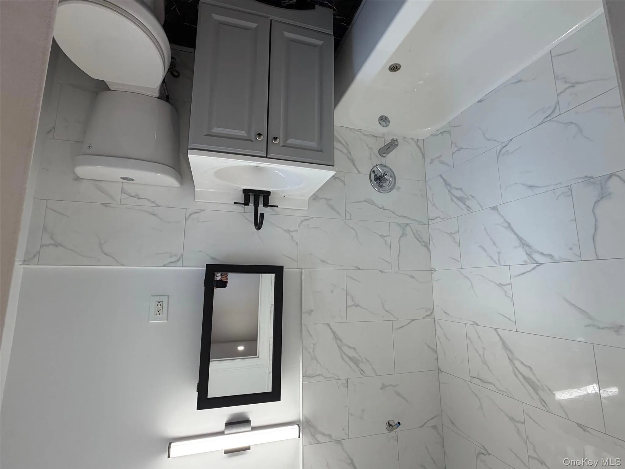 Full bathroom featuring tile walls, vanity, shower / bath combination, and wainscoting Full bathroom featuring tile walls, vanity, shower / bath combination, and wainscoting