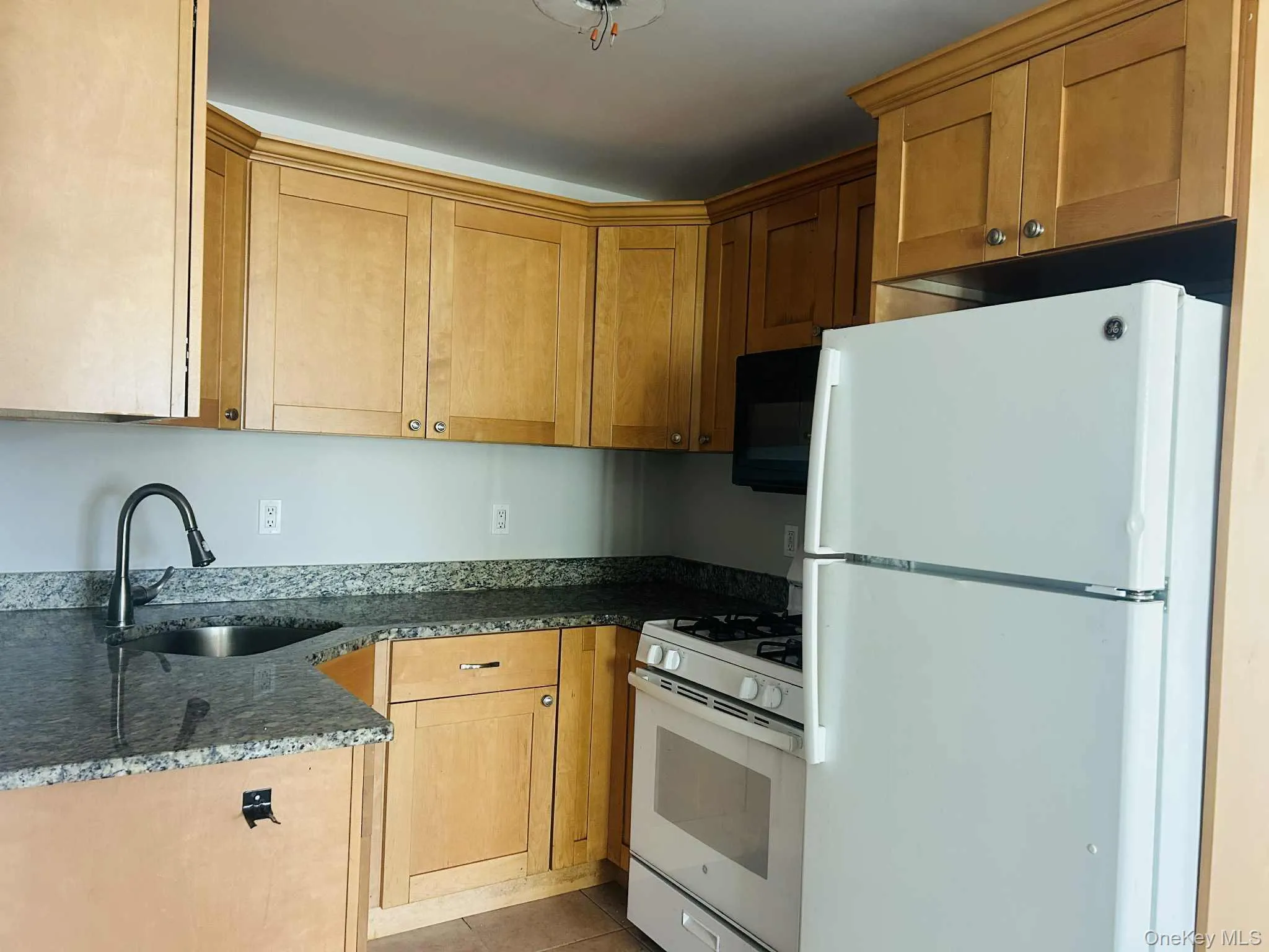 Kitchen with white appliances, dark stone counters, light tile patterned floors, and brown cabinets Kitchen with white appliances, dark stone counters, light tile patterned floors, and brown cabinets