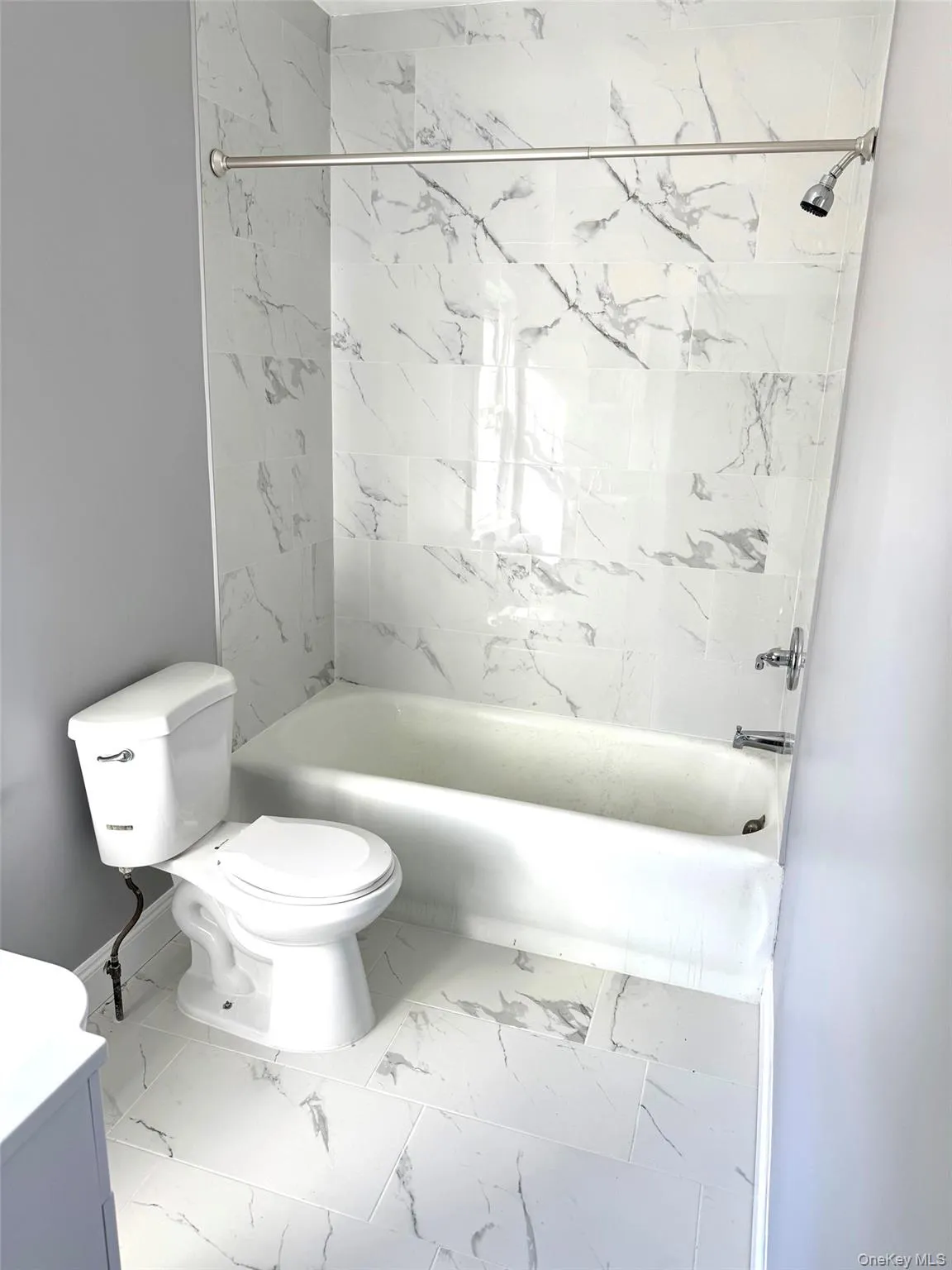 Bathroom featuring a combined bath / shower with marble appearance, vanity, and light marble finish flooring Bathroom featuring a combined bath / shower with marble appearance, vanity, and light marble finish flooring