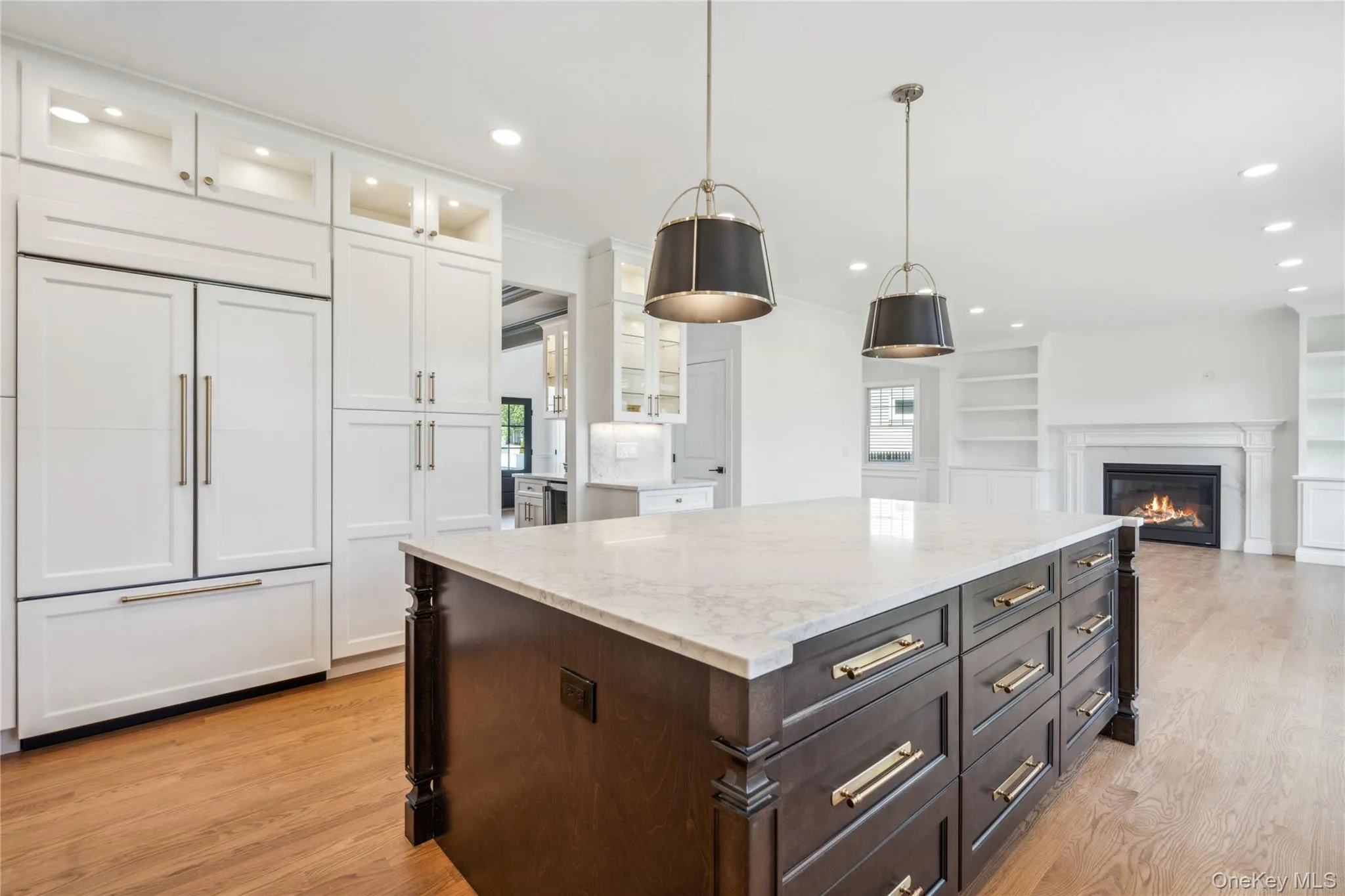 Kitchen with dark brown cabinetry, light stone countertops, white cabinets, a glass covered fireplace, and light wood-style floors Kitchen with dark brown cabinetry, light stone countertops, white cabinets, a glass covered fireplace, and light wood-style floors