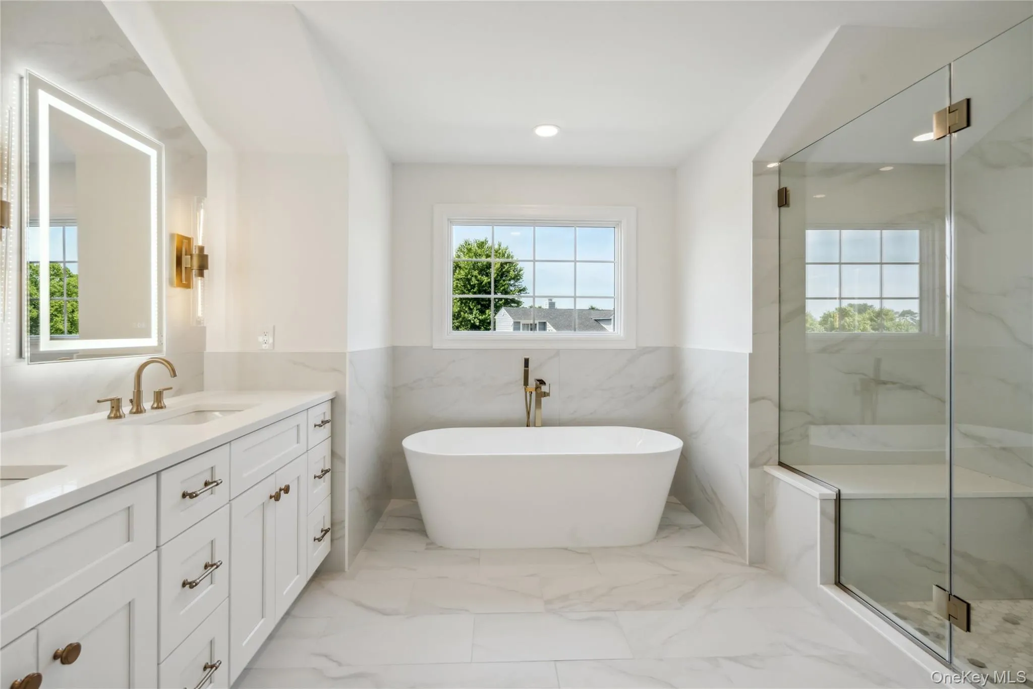 Bathroom featuring tile walls, double vanity, light marble finish flooring, a marble finish shower, and a freestanding tub Bathroom featuring tile walls, double vanity, light marble finish flooring, a marble finish shower, and a freestanding tub