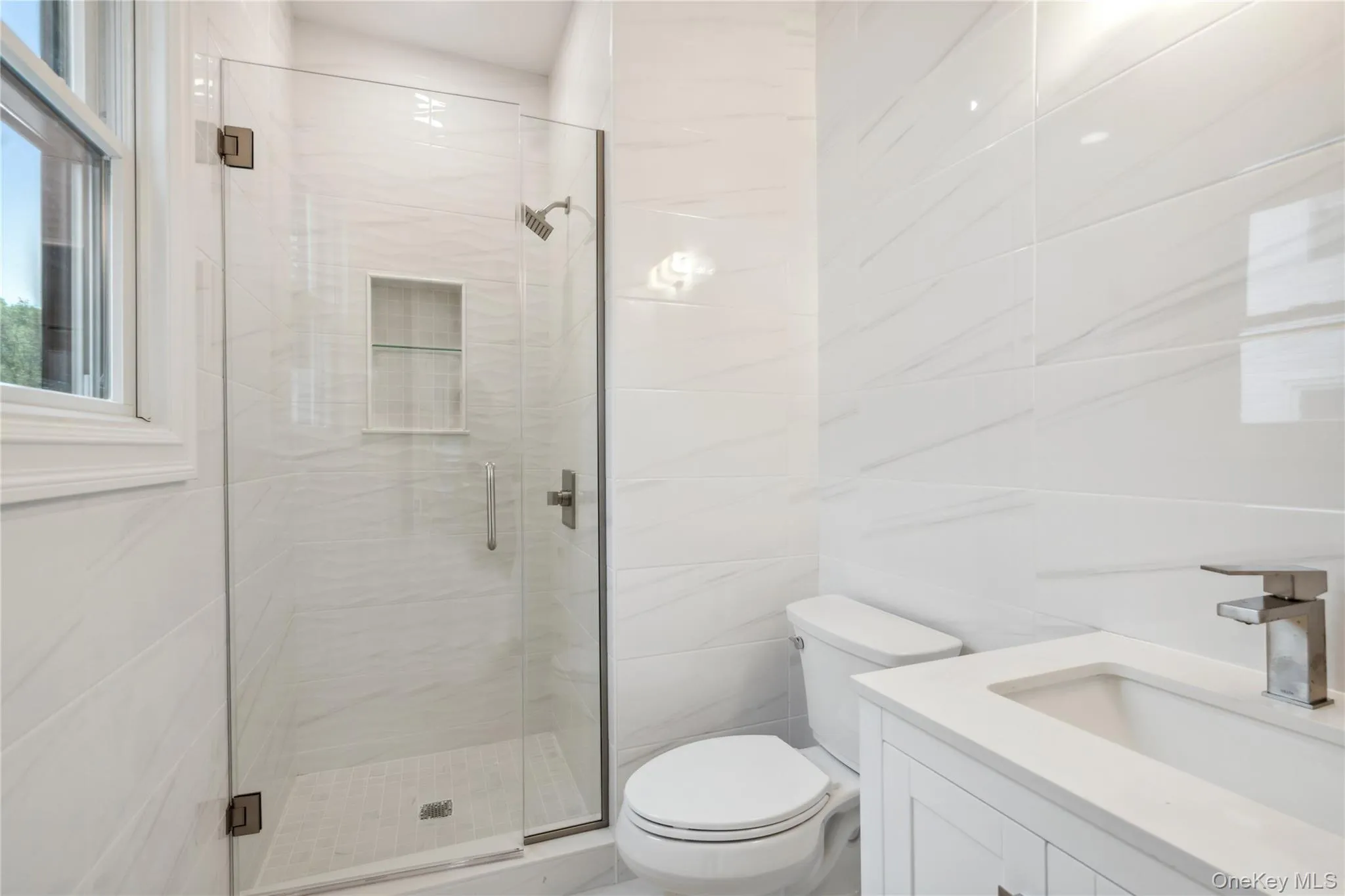 Full bathroom featuring a marble finish shower, vanity, and tile walls Full bathroom featuring a marble finish shower, vanity, and tile walls