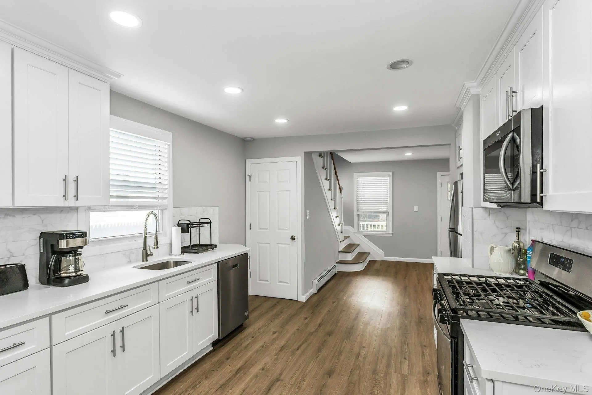 Kitchen with backsplash, stainless steel appliances, white cabinetry, recessed lighting, and dark wood-style flooring Kitchen with backsplash, stainless steel appliances, white cabinetry, recessed lighting, and dark wood-style flooring