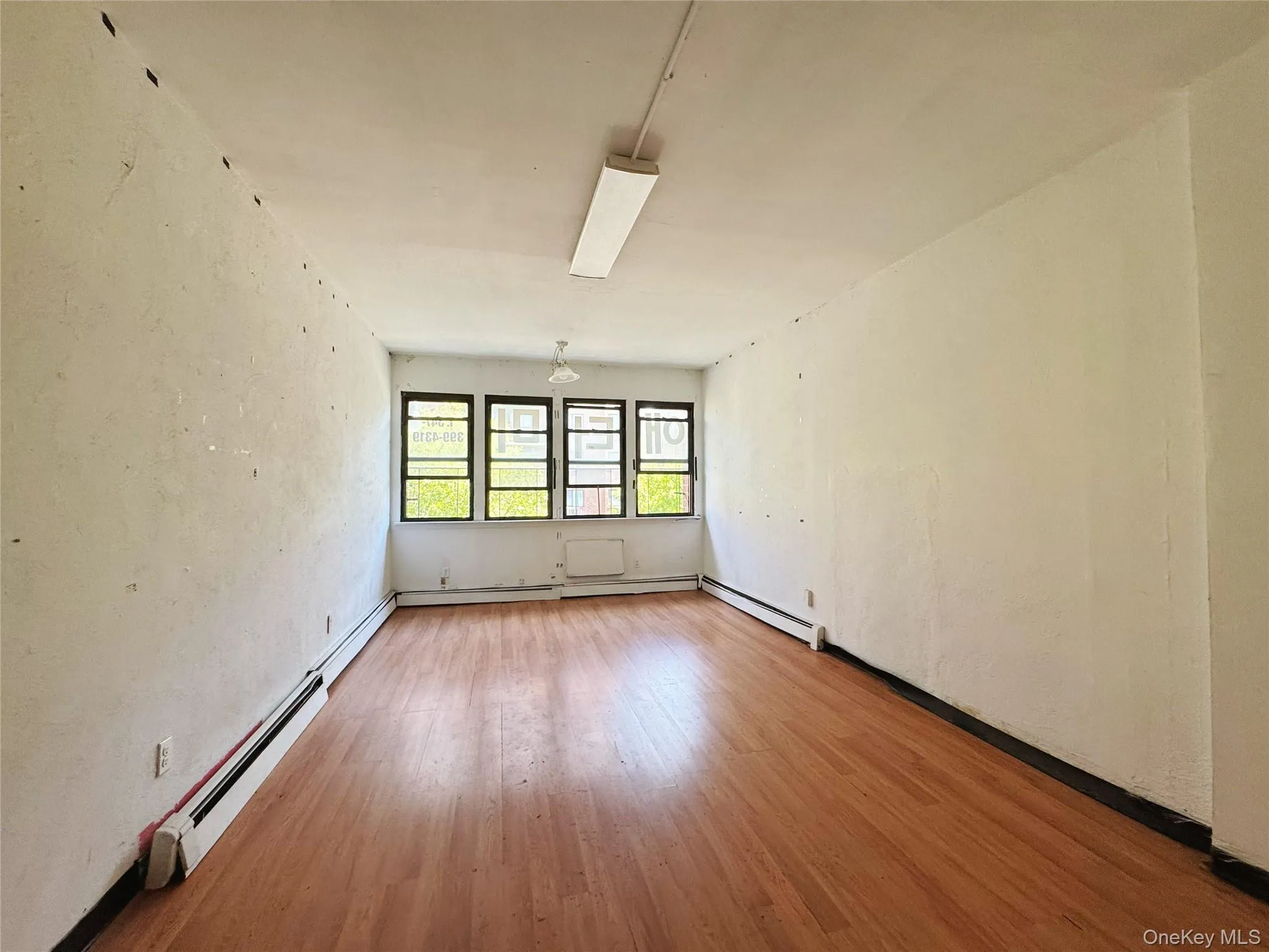 Unfurnished room featuring a textured wall, baseboard heating, and light wood finished floors Unfurnished room featuring a textured wall, baseboard heating, and light wood finished floors