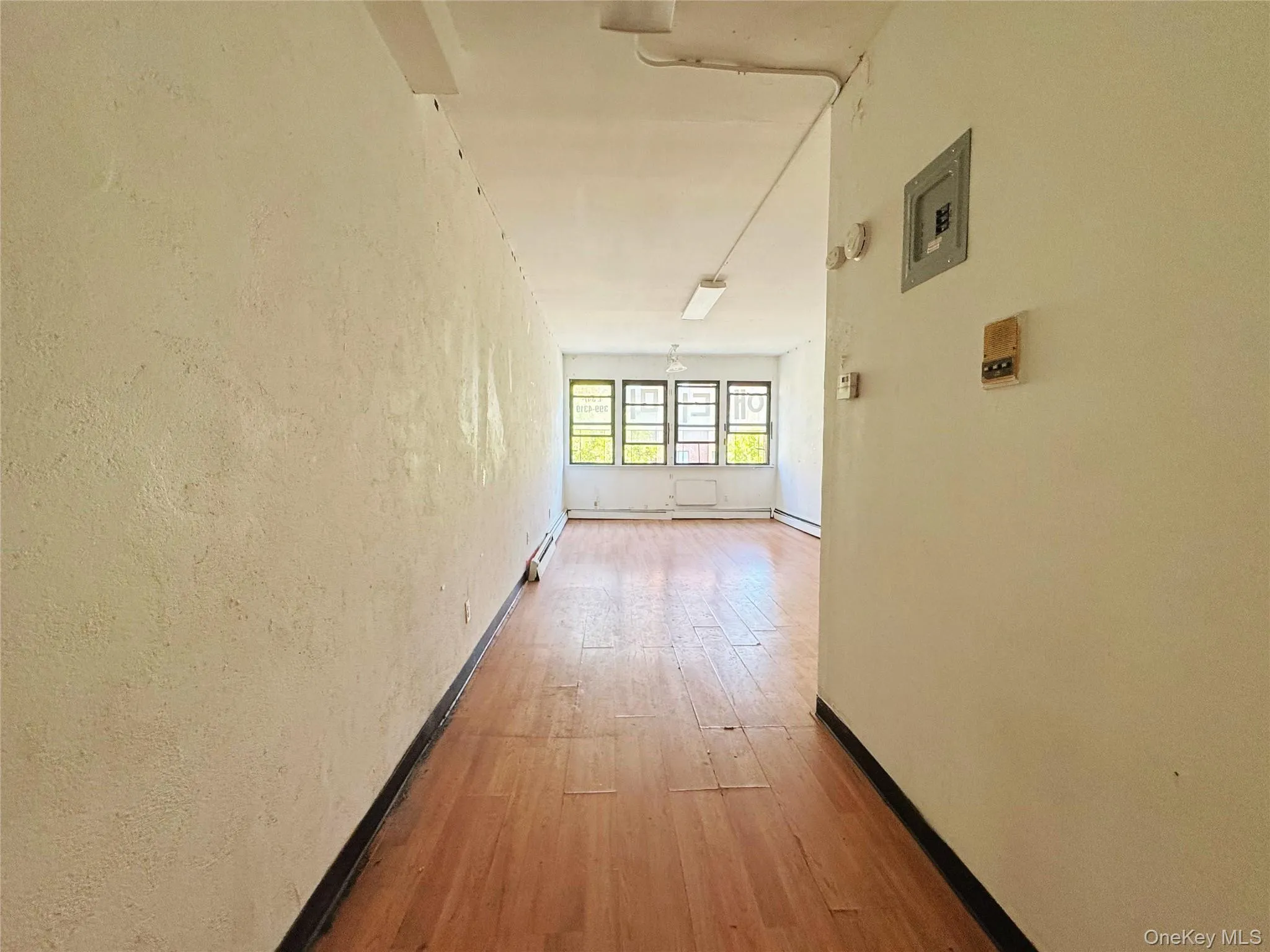 Hallway featuring light wood-type flooring, a textured wall, and electric panel Hallway featuring light wood-type flooring, a textured wall, and electric panel