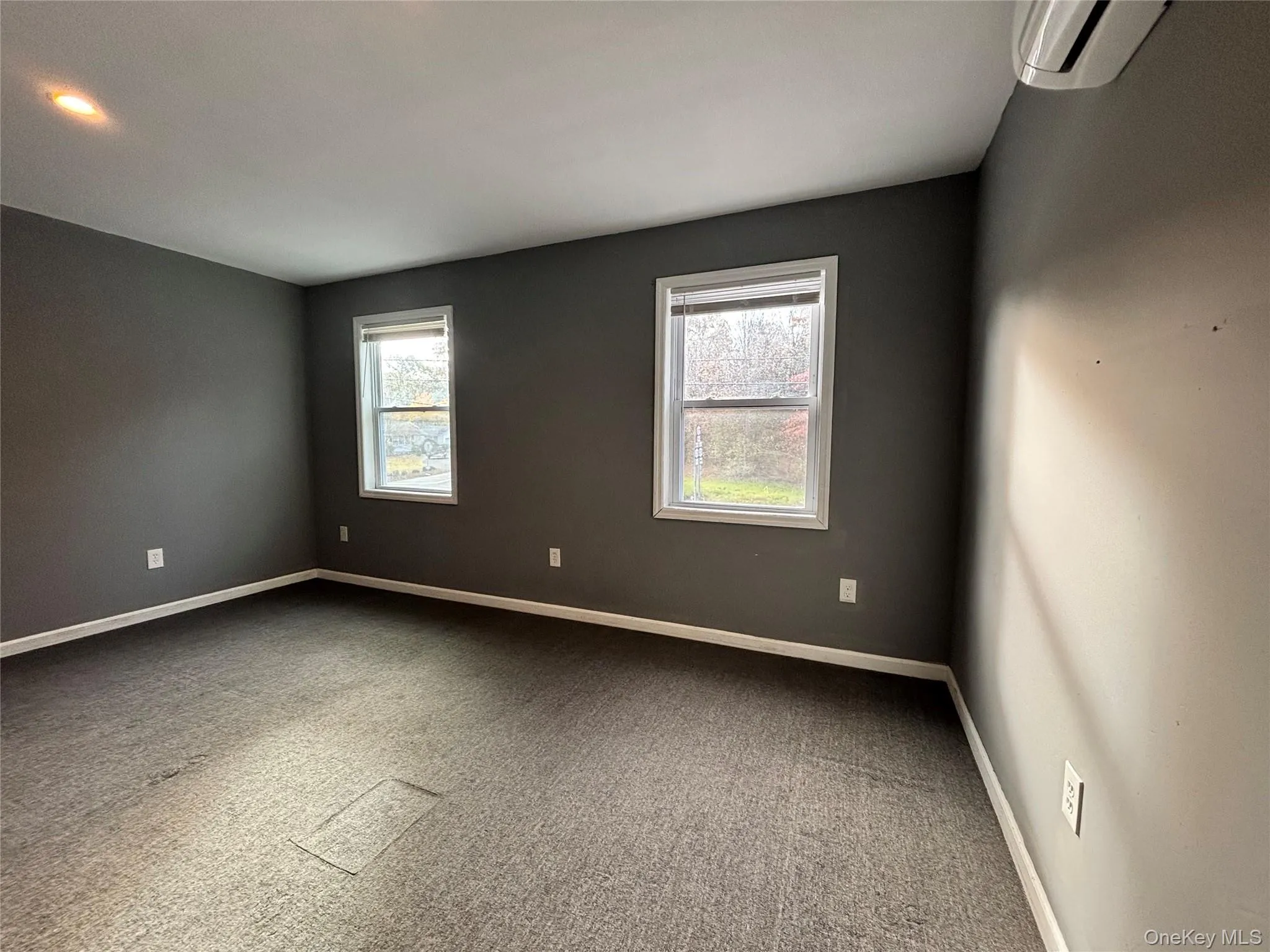 Carpeted spare room with baseboards and a wall mounted air conditioner Carpeted spare room with baseboards and a wall mounted air conditioner
