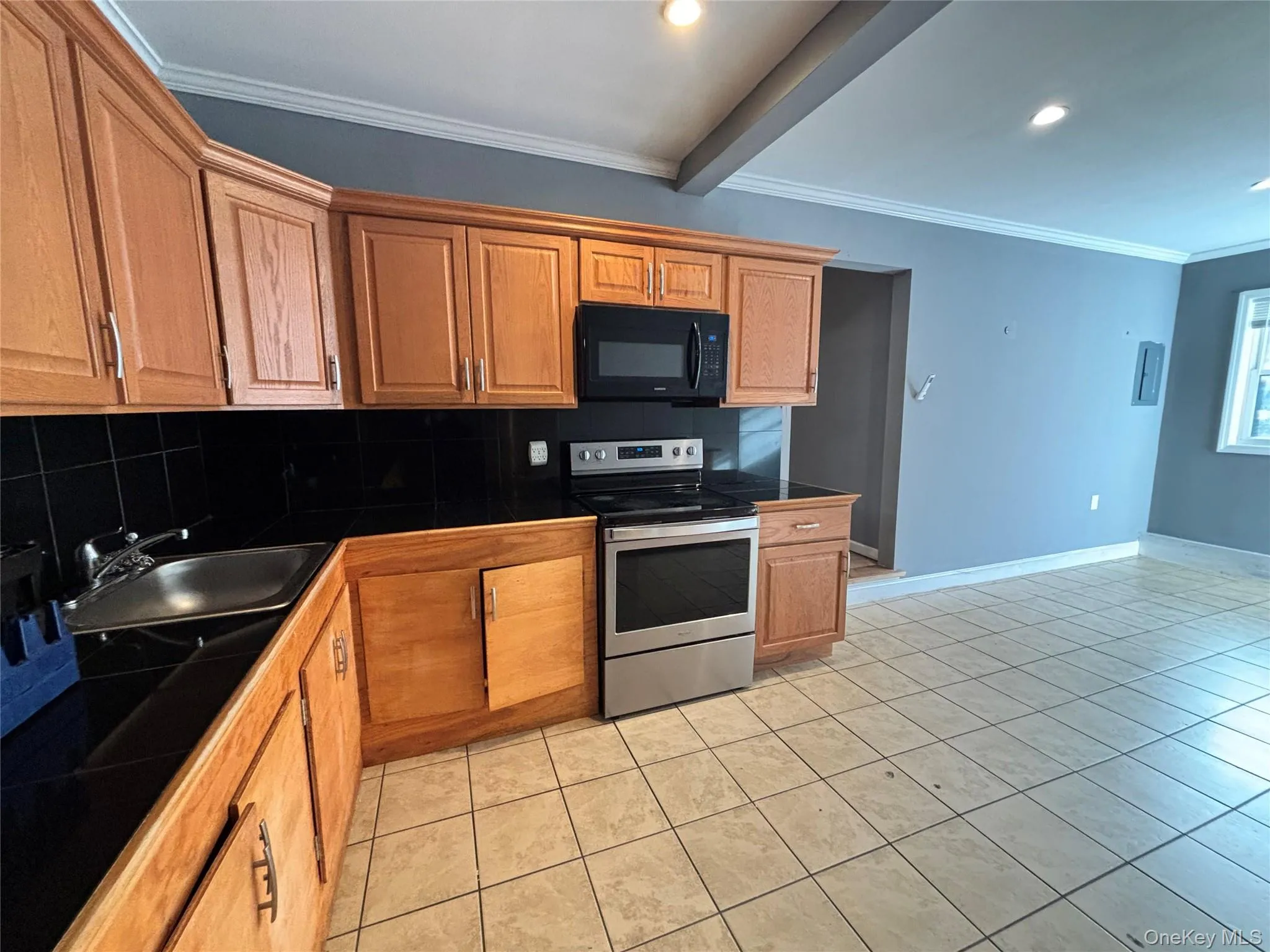 Kitchen featuring tasteful backsplash, crown molding, electric range, light tile patterned floors, and black microwave Kitchen featuring tasteful backsplash, crown molding, electric range, light tile patterned floors, and black microwave