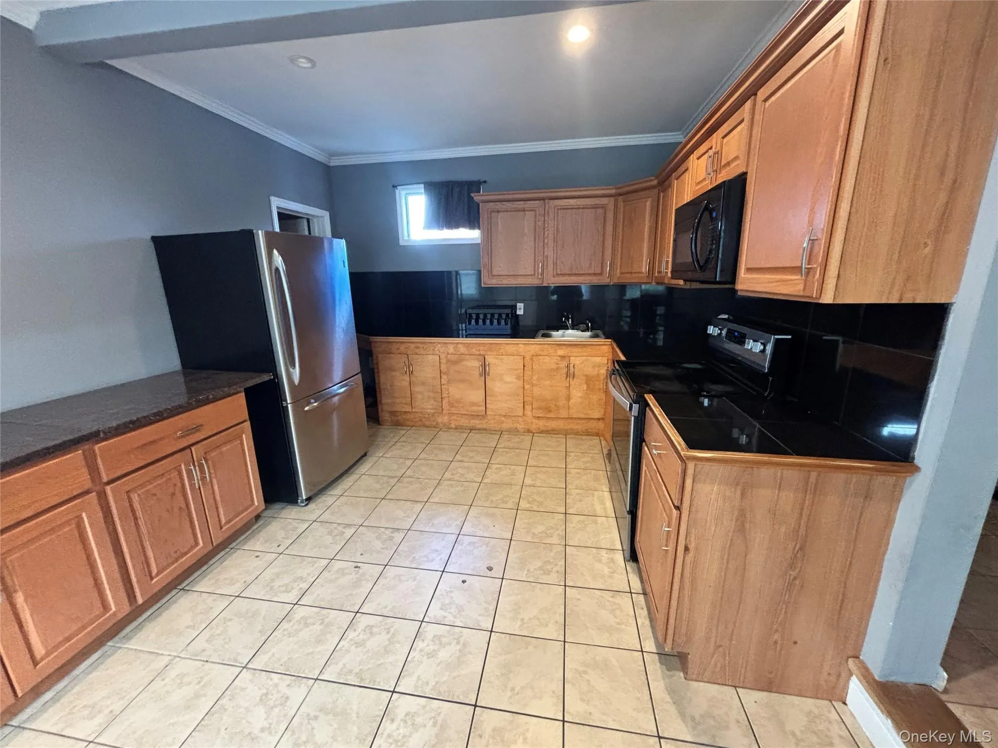Kitchen featuring range with electric stovetop, ornamental molding, freestanding refrigerator, brown cabinets, and dark countertops Kitchen featuring range with electric stovetop, ornamental molding, freestanding refrigerator, brown cabinets, and dark countertops