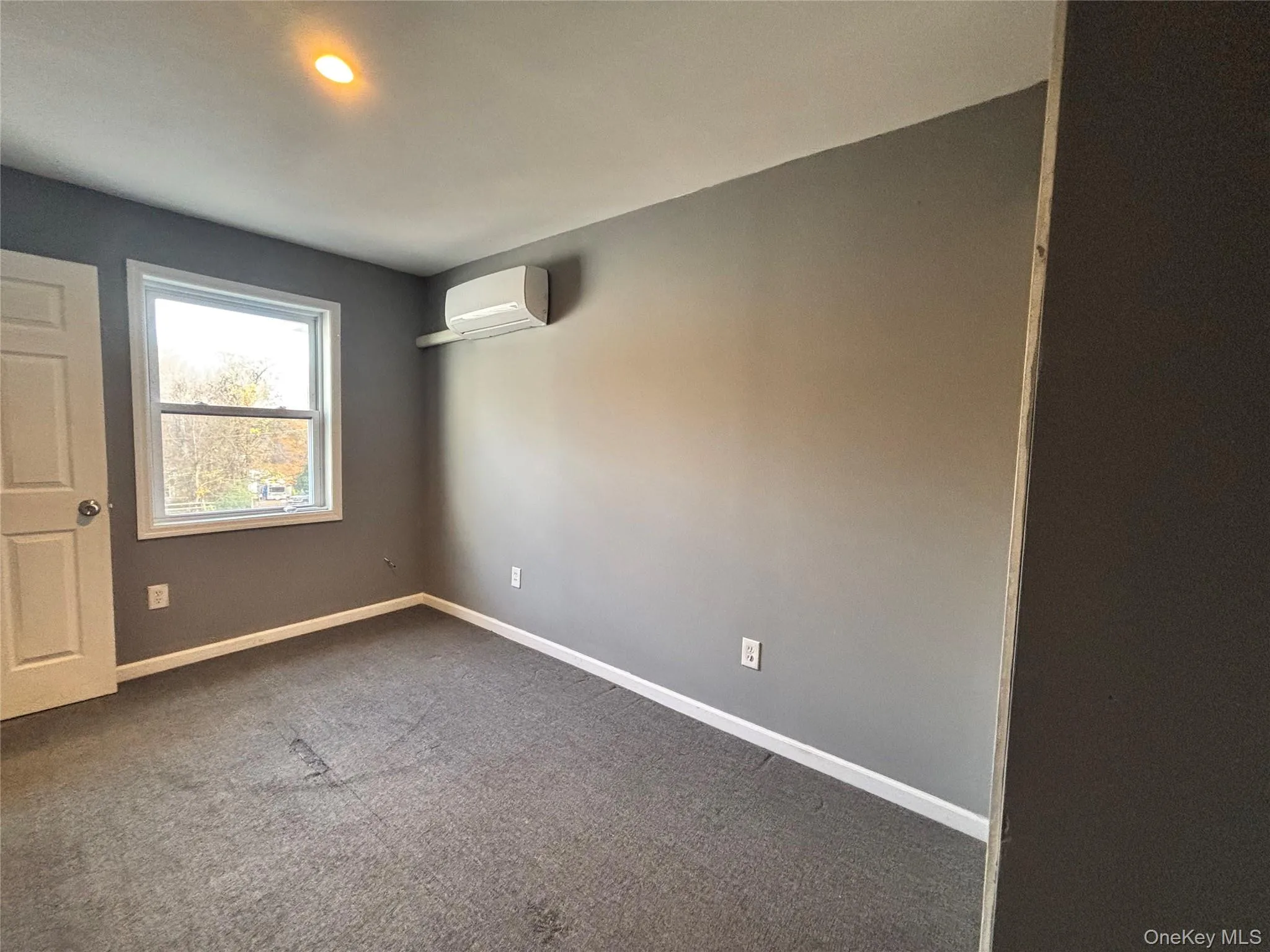 Empty room with dark carpet, an AC wall unit, and recessed lighting Empty room with dark carpet, an AC wall unit, and recessed lighting