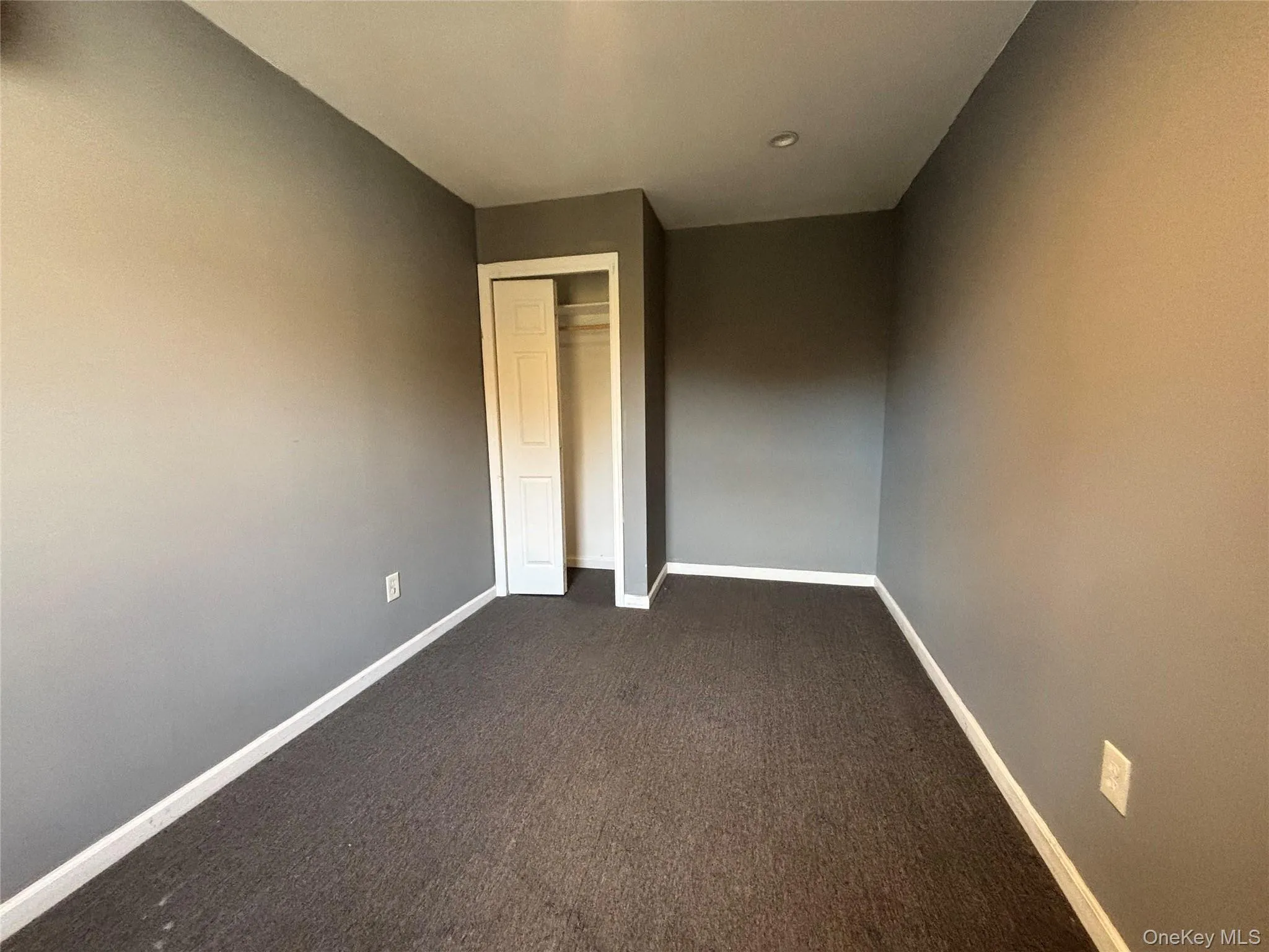 Unfurnished bedroom featuring dark carpet and a closet Unfurnished bedroom featuring dark carpet and a closet