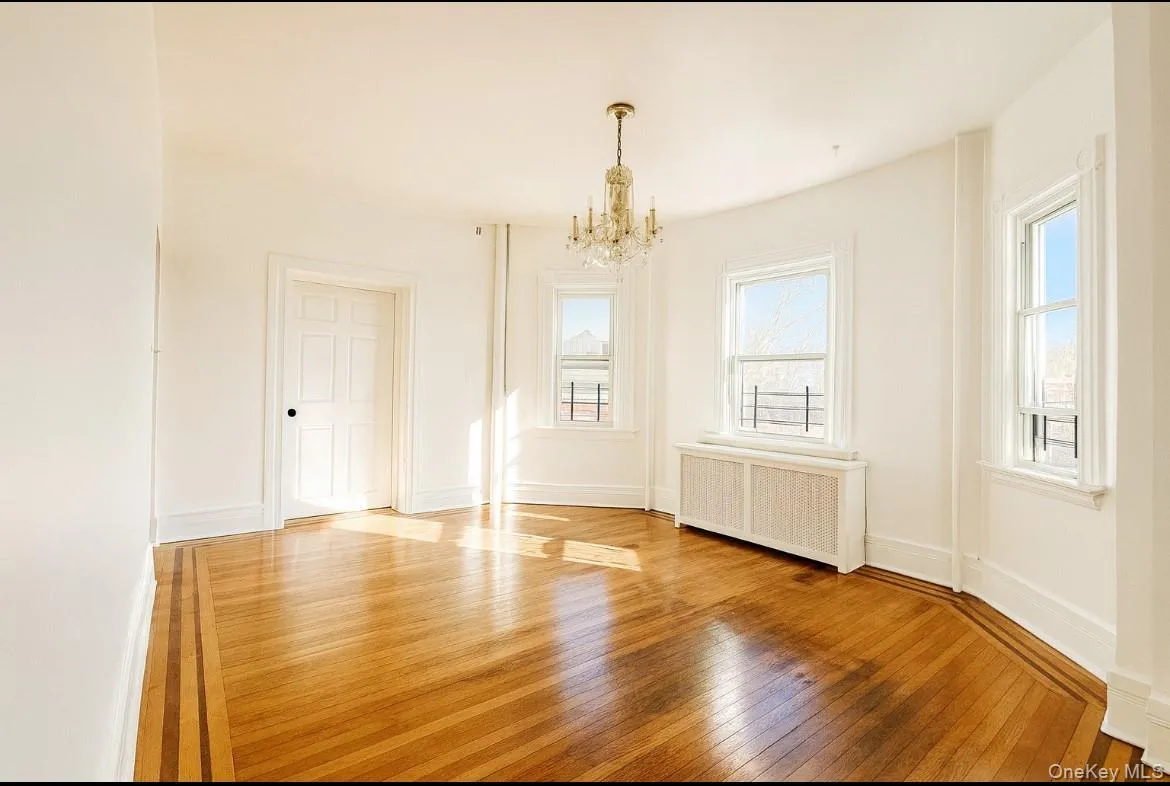 Unfurnished dining area with hardwood / wood-style floors, radiator, healthy amount of natural light, and a chandelier Unfurnished dining area with hardwood / wood-style floors, radiator, healthy amount of natural light, and a chandelier