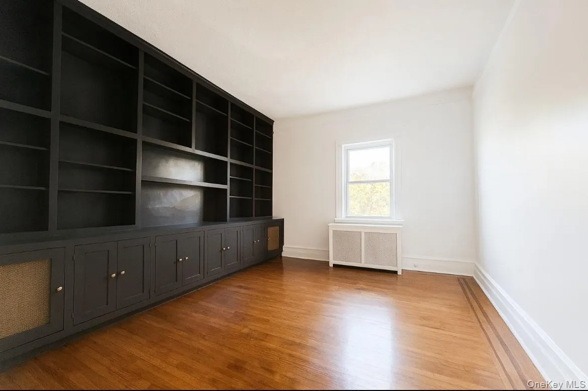 Spare room featuring radiator, light wood-type flooring, and built in features Spare room featuring radiator, light wood-type flooring, and built in features