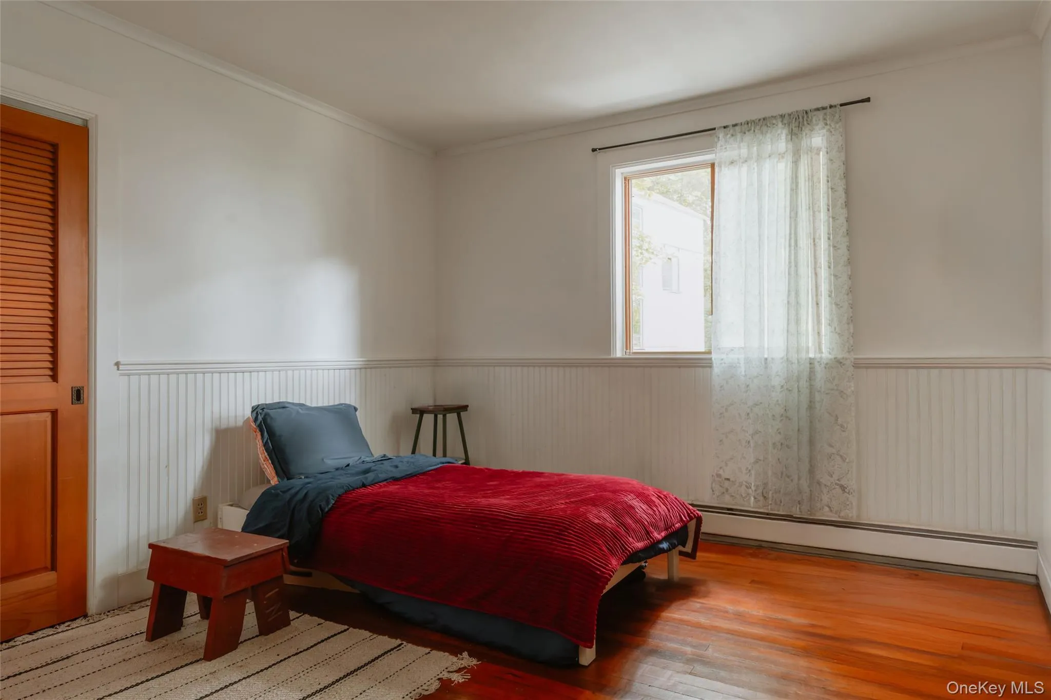 Bedroom featuring wood finished floors, a baseboard heating unit, crown molding, and wainscoting Bedroom featuring wood finished floors, a baseboard heating unit, crown molding, and wainscoting