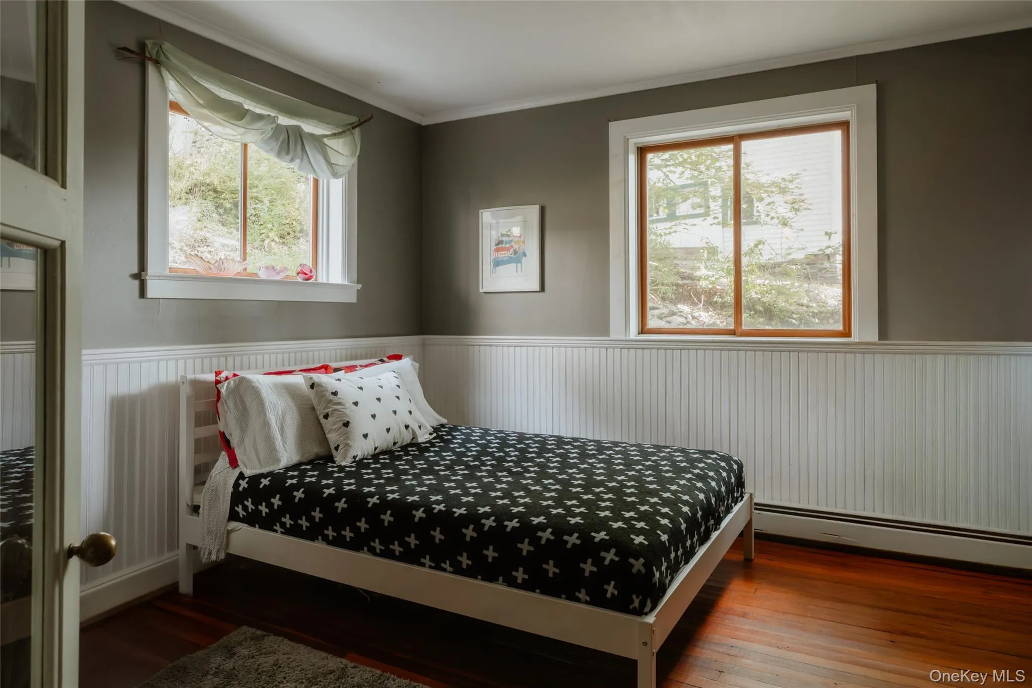 Bedroom with ornamental molding, a baseboard radiator, dark wood-style floors, and a wainscoted wall Bedroom with ornamental molding, a baseboard radiator, dark wood-style floors, and a wainscoted wall